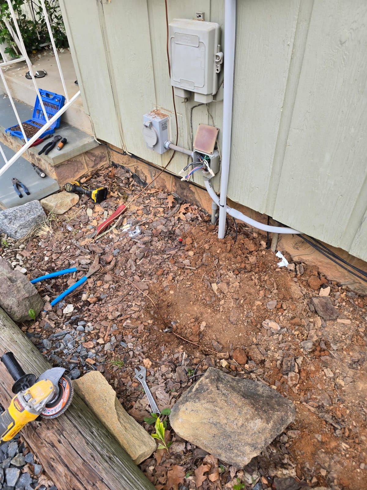 Excavated dirt and debris beside a house exterior with utility meter and pipes visible