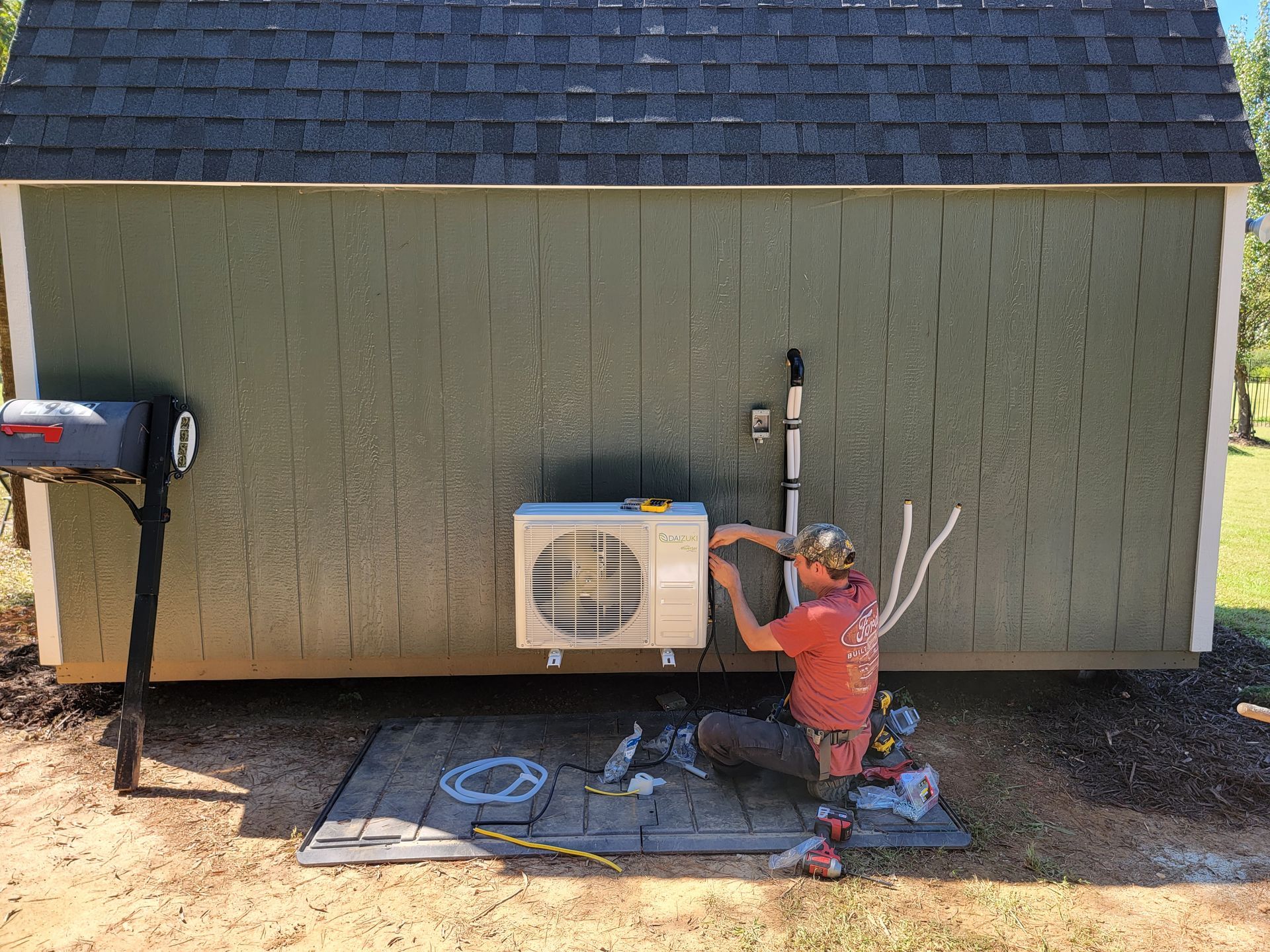 Outdoor HVAC unit with a technician working on pipes beside a green building