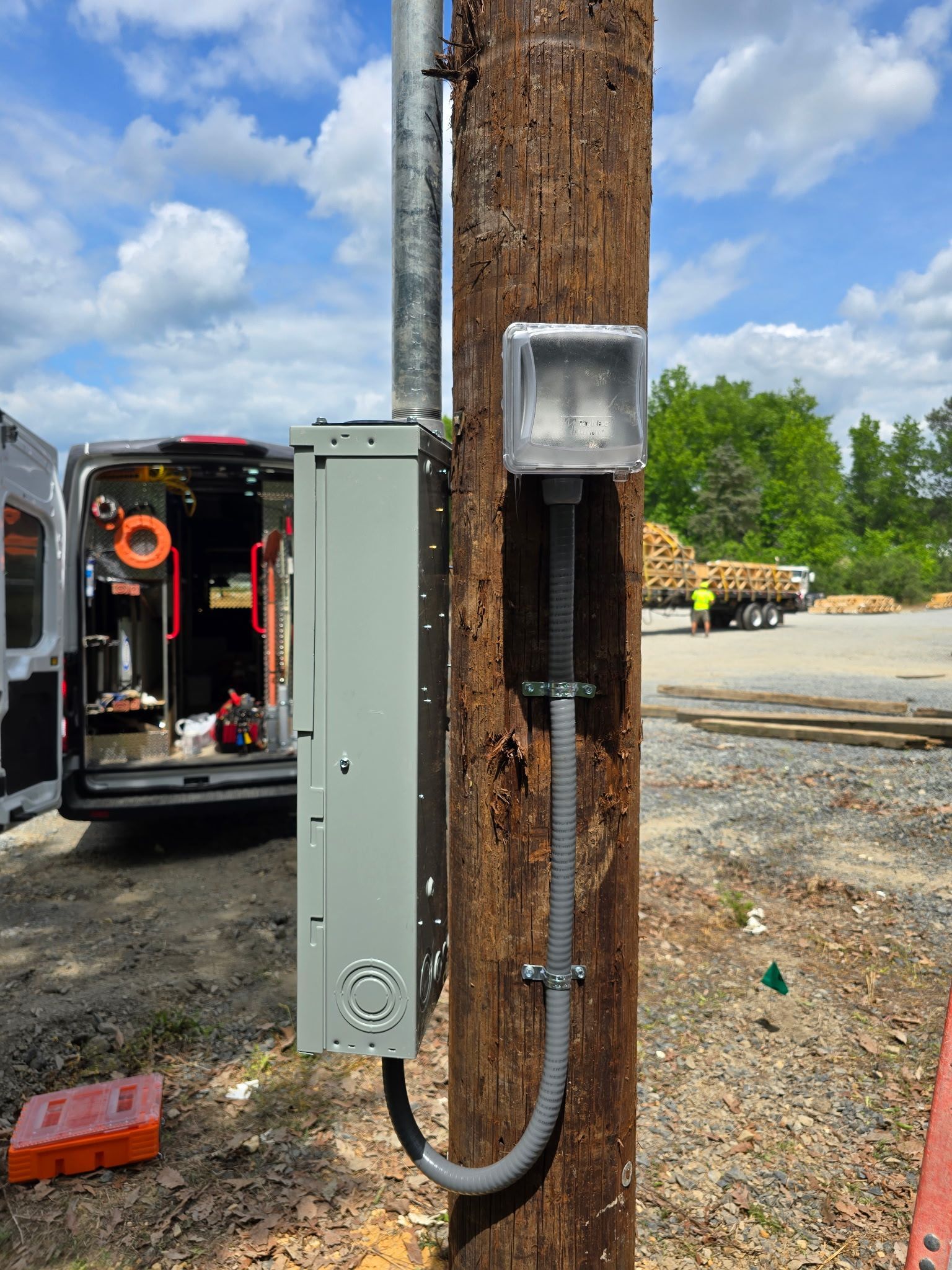 Electrical service box mounted on a wooden utility pole beside a work van and parking lot