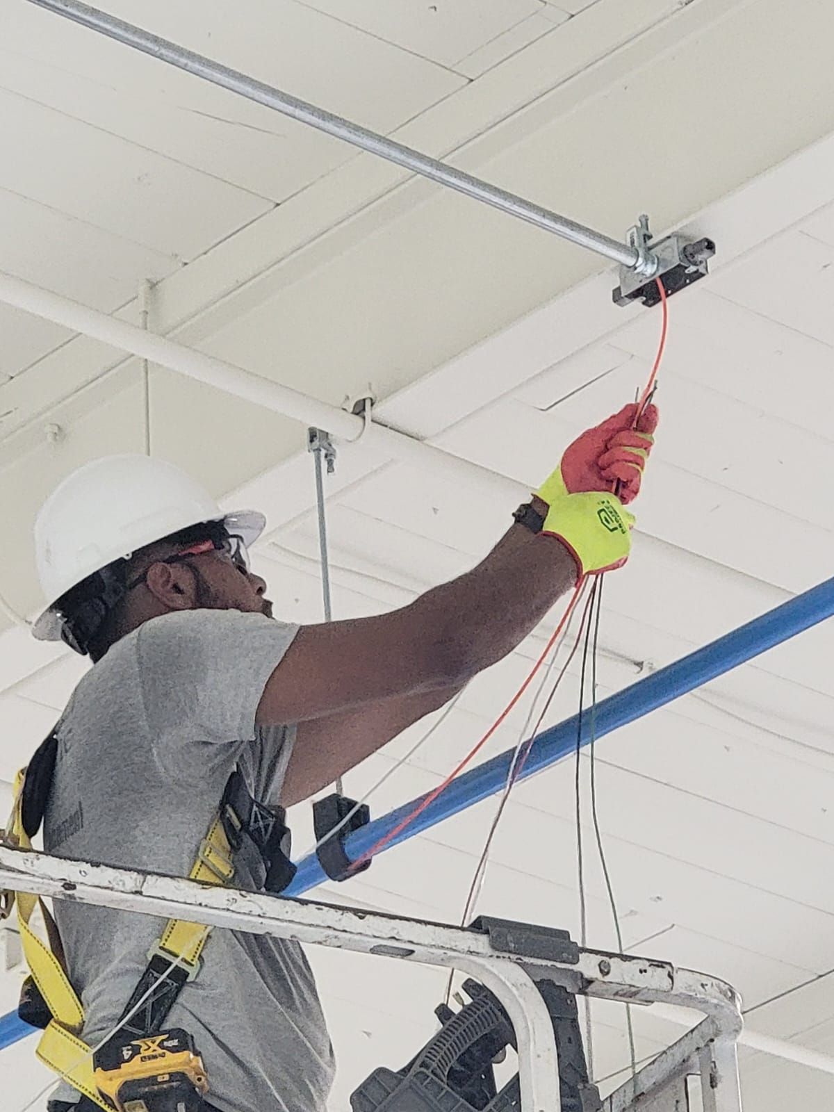 Worker in a hard hat and safety harness repairing overhead ceiling fixtures from a lift.