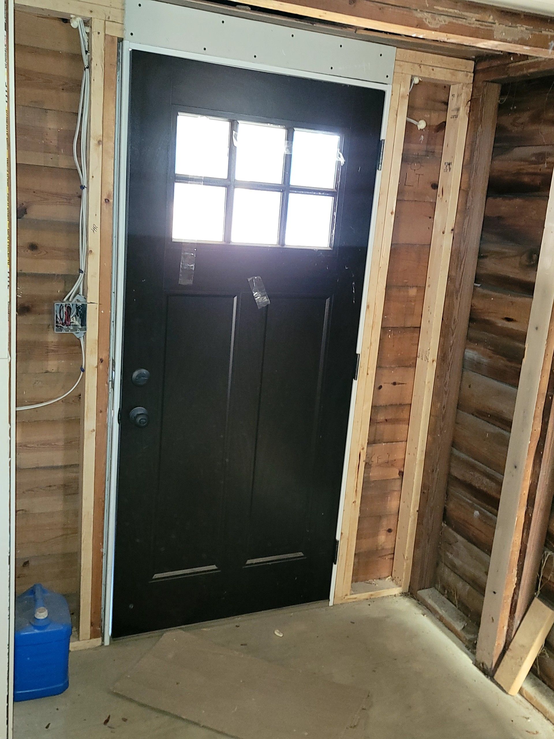 Black door with small window in a raw wood-framed entryway under construction