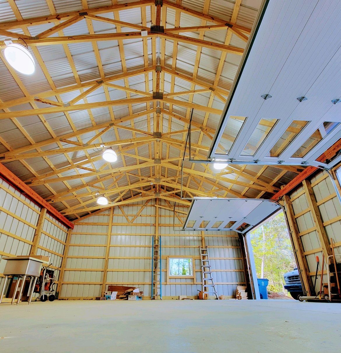 Empty large workshop interior with exposed wooden trusses, metal walls, and open garage doors