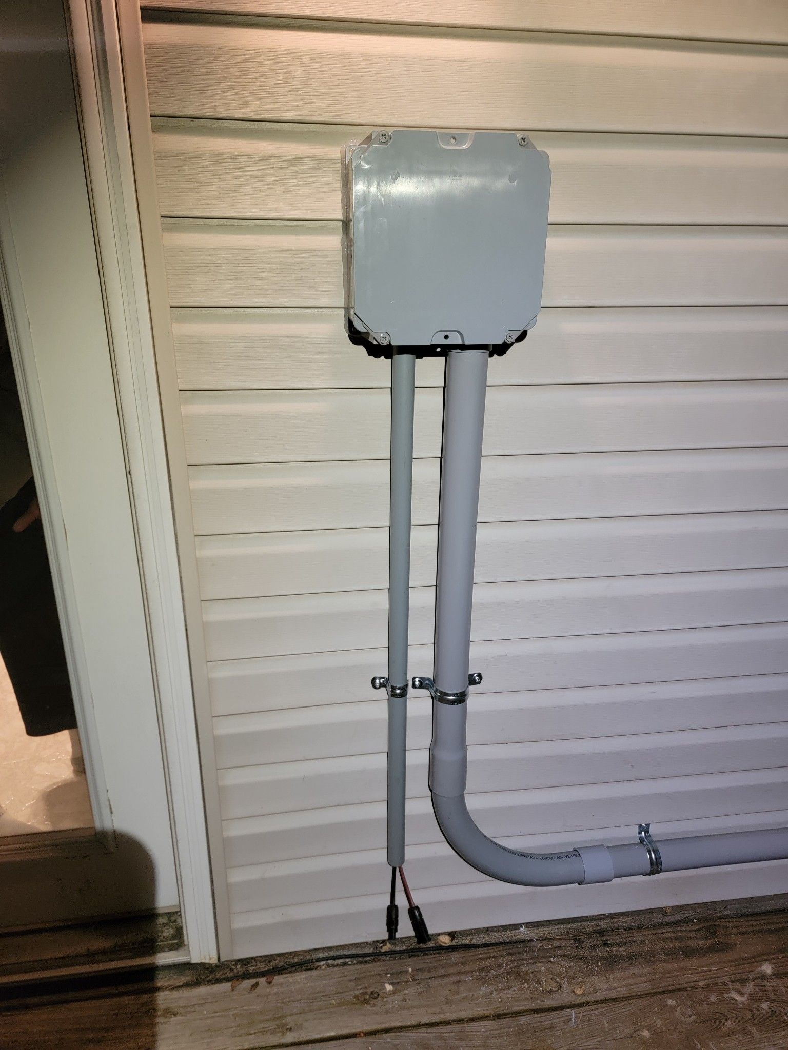 Gray electrical utility box with conduit pipes mounted on an exterior wall near the ground