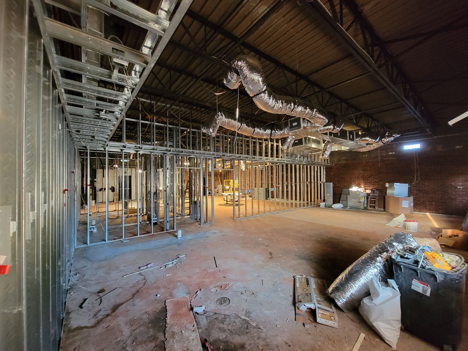 Interior construction site with exposed framing, ductwork, and debris on the floor