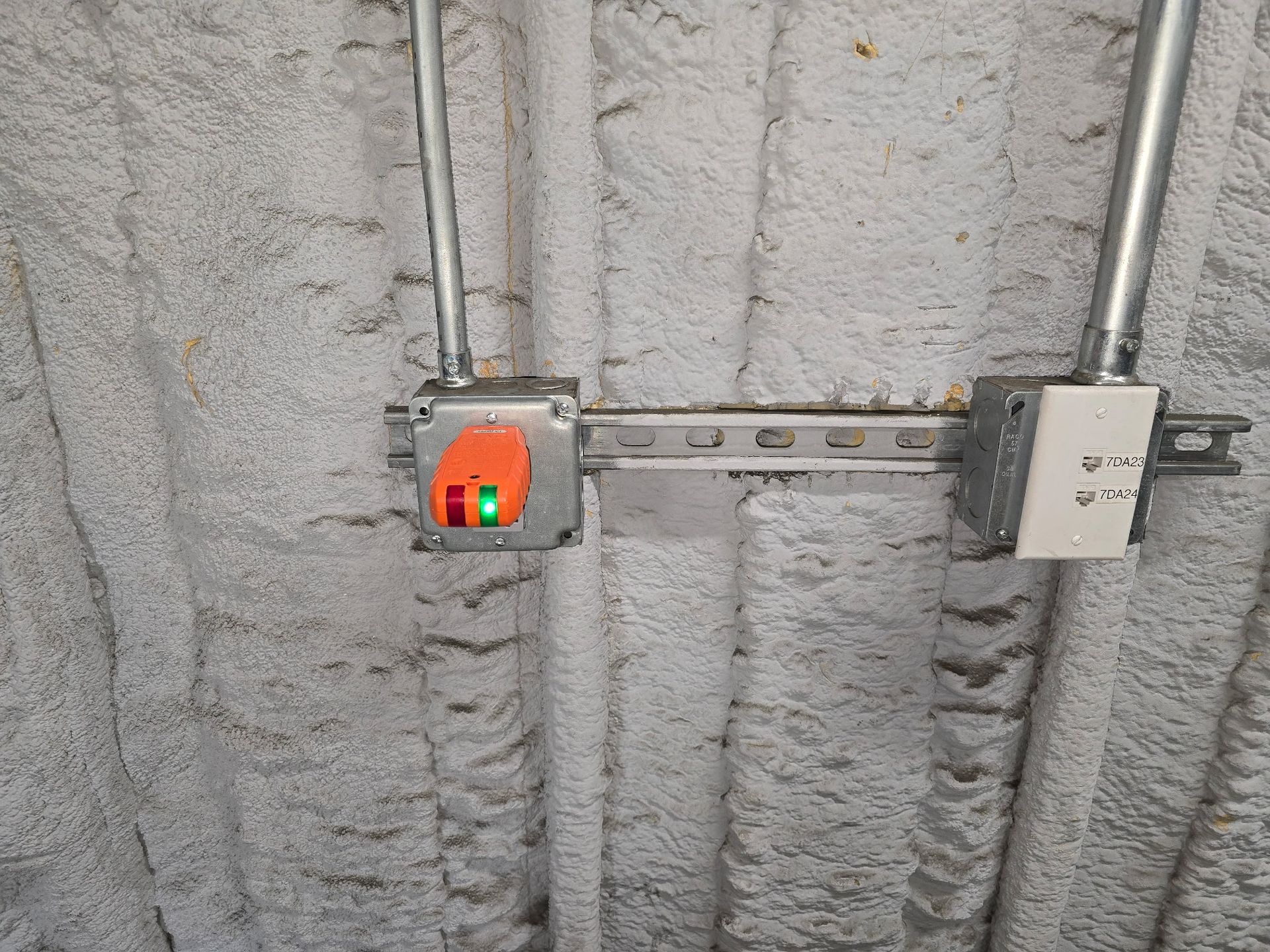 Electrical conduit and junction boxes mounted on a textured gray concrete wall, with one orange-lit box.