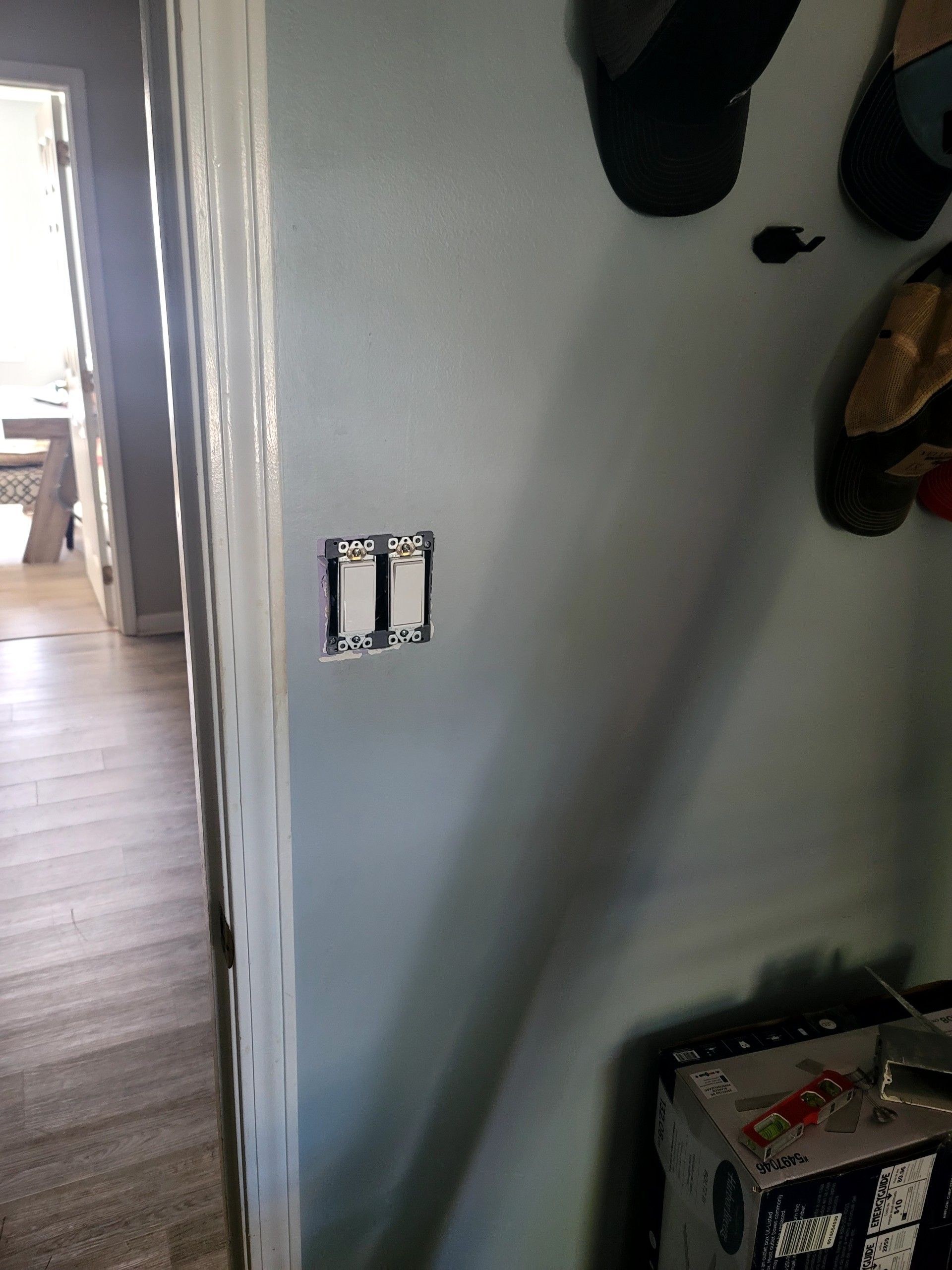 Partially painted hallway wall with a light switch opening and hanging tools nearby