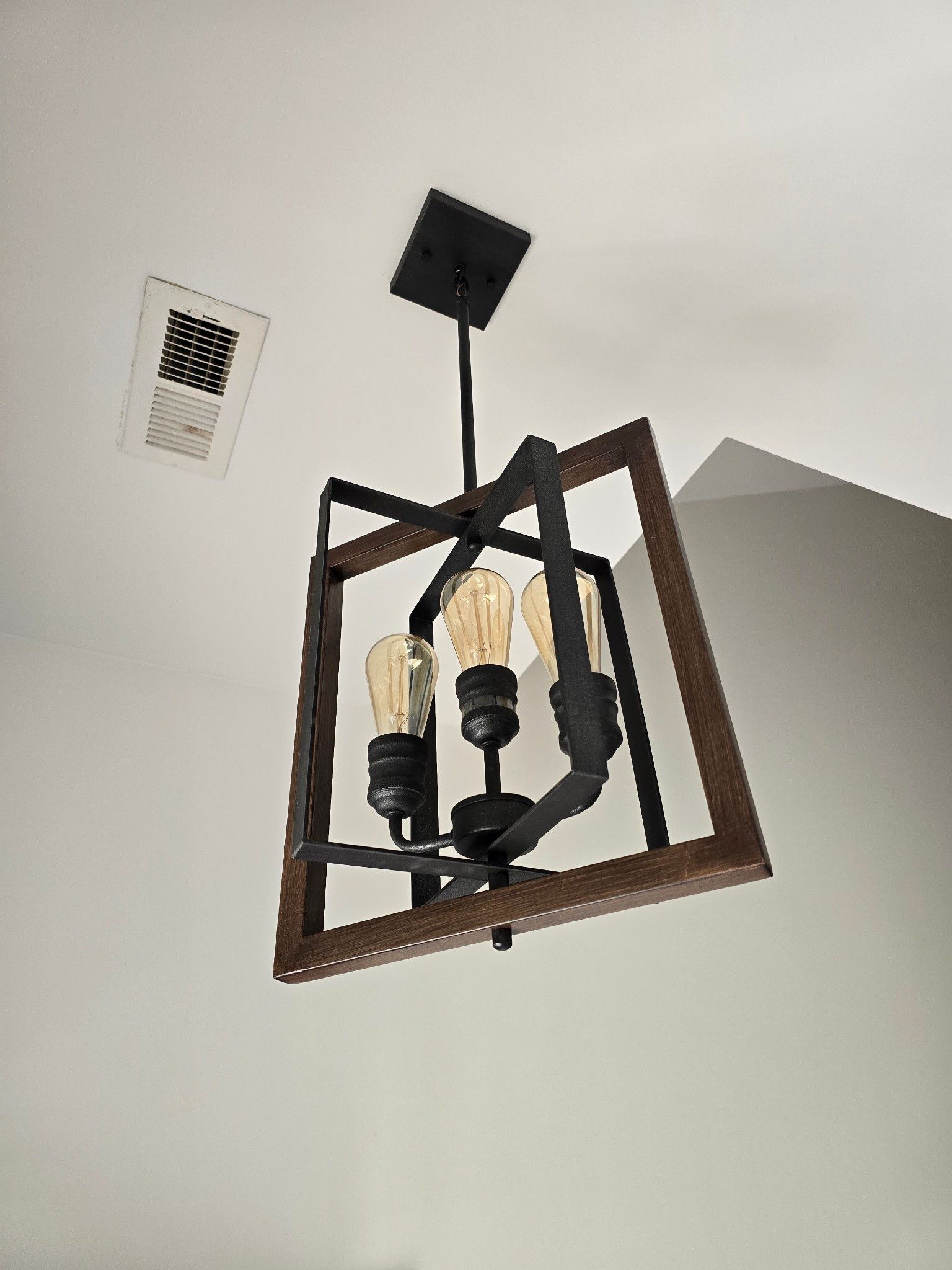 Ceiling light fixture with dark wood frame and three exposed bulbs against a white ceiling