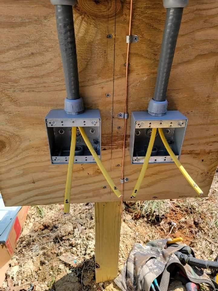 Two gray electrical boxes on plywood with yellow grounding wires at a construction site