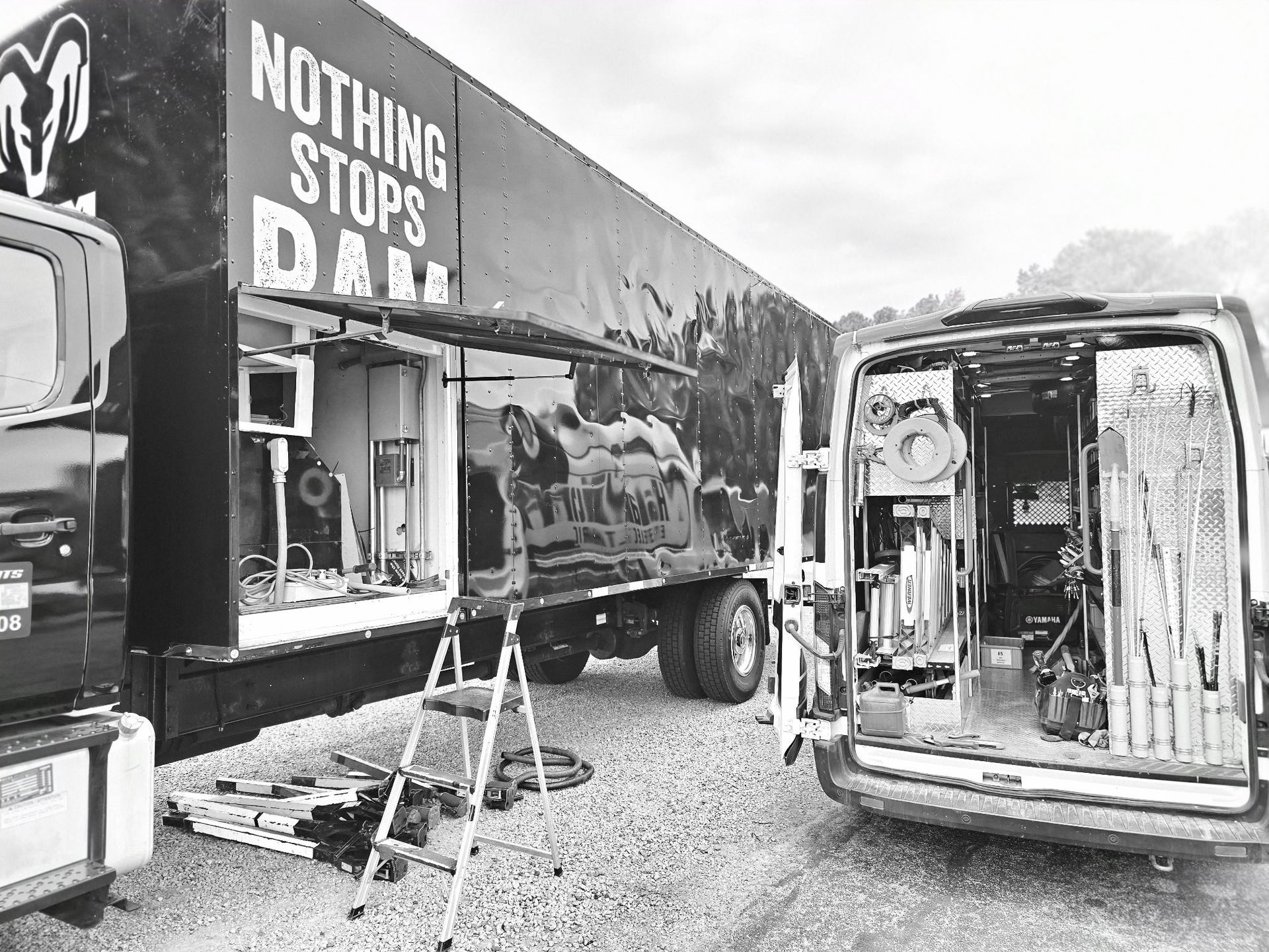 Black-and-white photo of a truck body with graffiti-style text and an open van on gravel lot