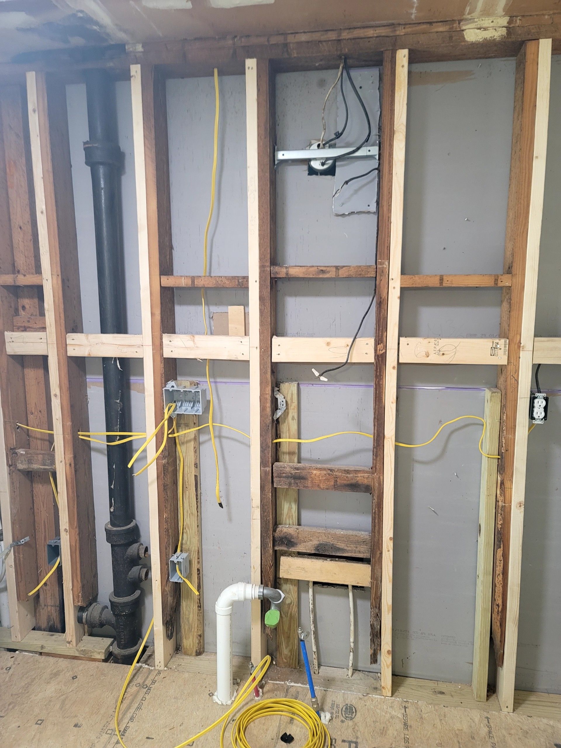 Open wall framing with exposed plumbing and electrical wiring in a room under construction