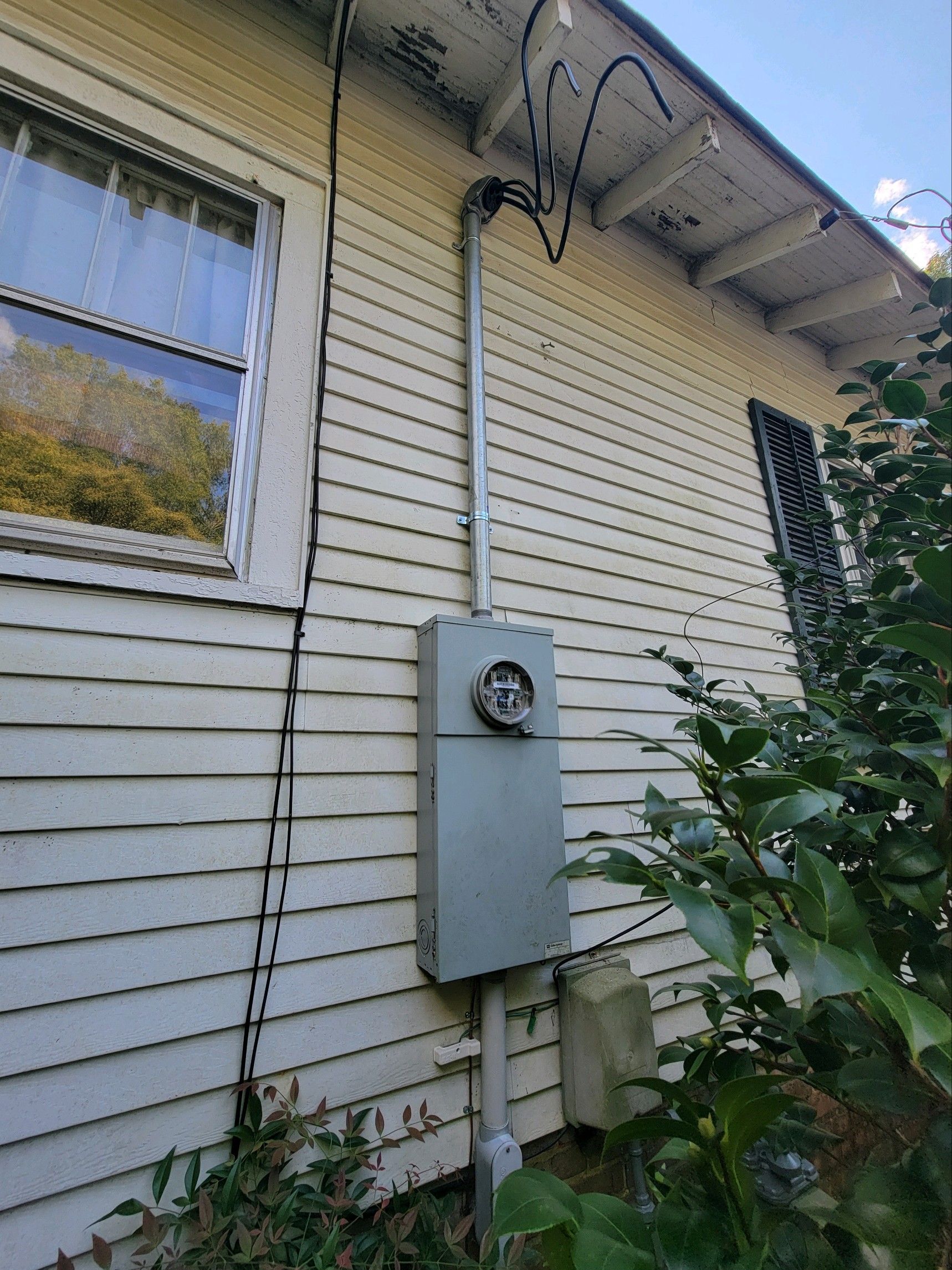 White house exterior with electrical meter box, window, and overhanging cables beside shrubs