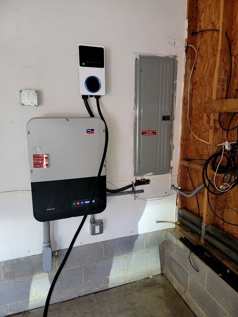 Electrical panels and utility boxes mounted on a basement wall, with exposed wiring and conduit.