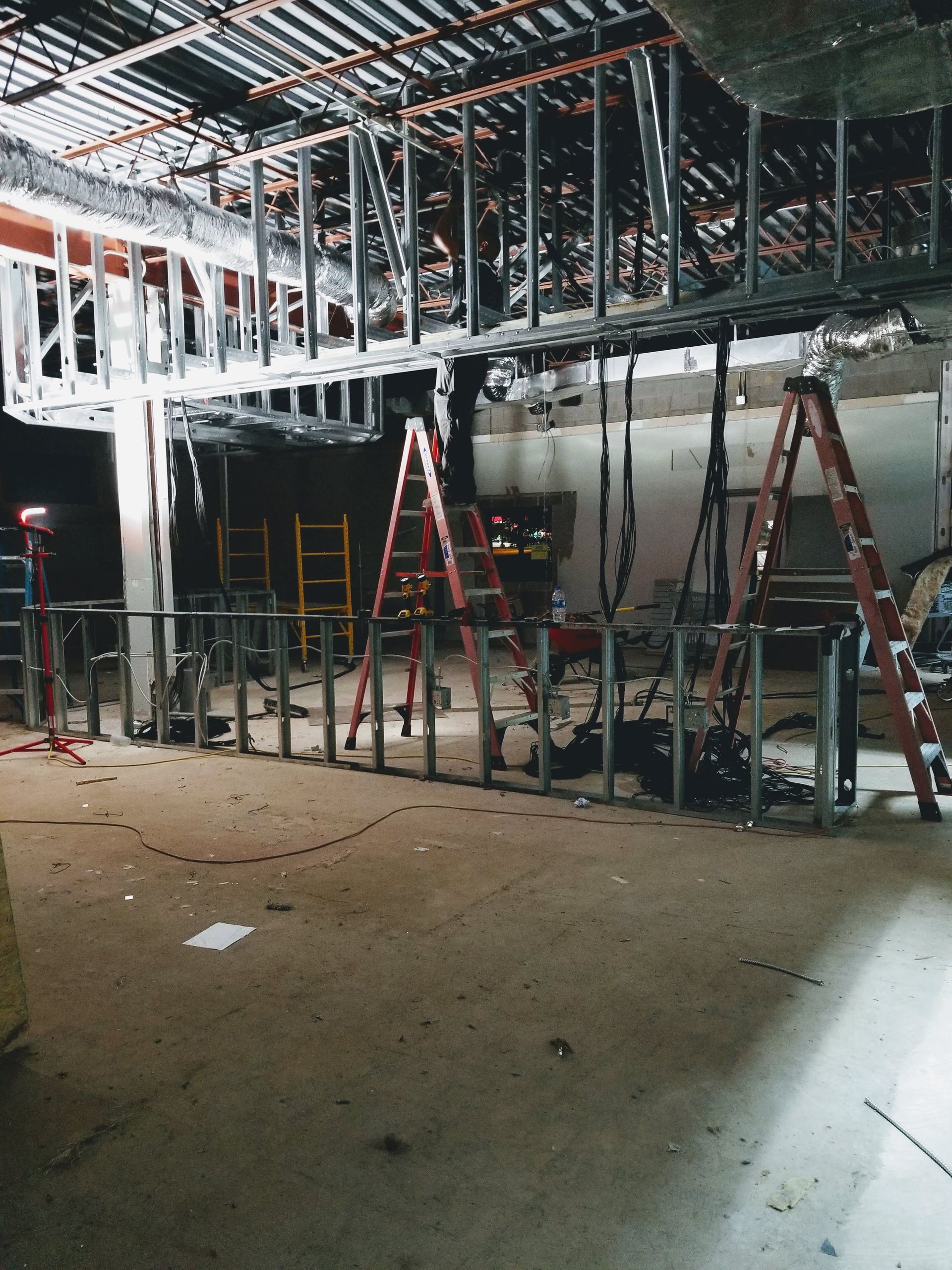 Construction site with ladders and scaffolding in a partially built interior, under exposed ceiling framing.