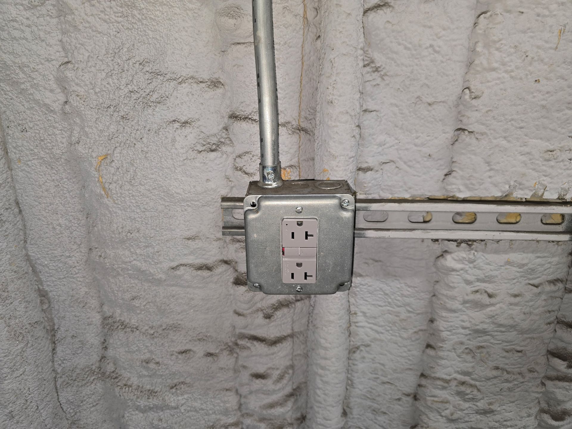 Electrical outlet and conduit mounted on a rough concrete wall.