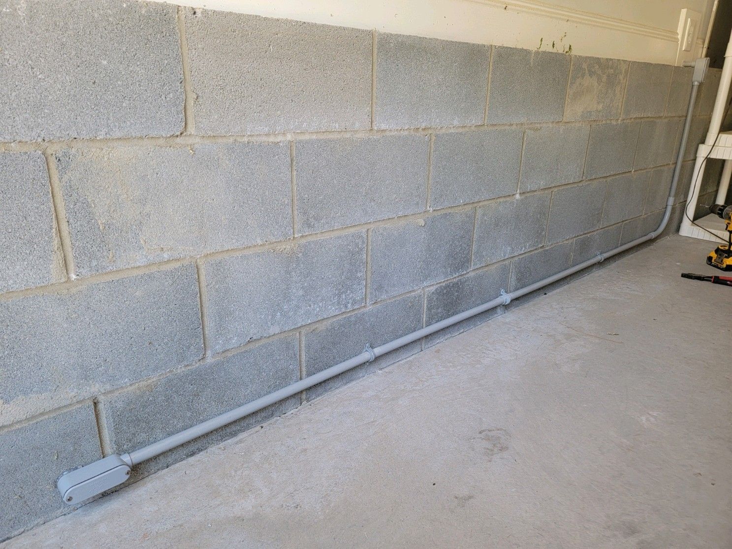 Basement wall with gray cinder blocks and a metal pipe along the floor.