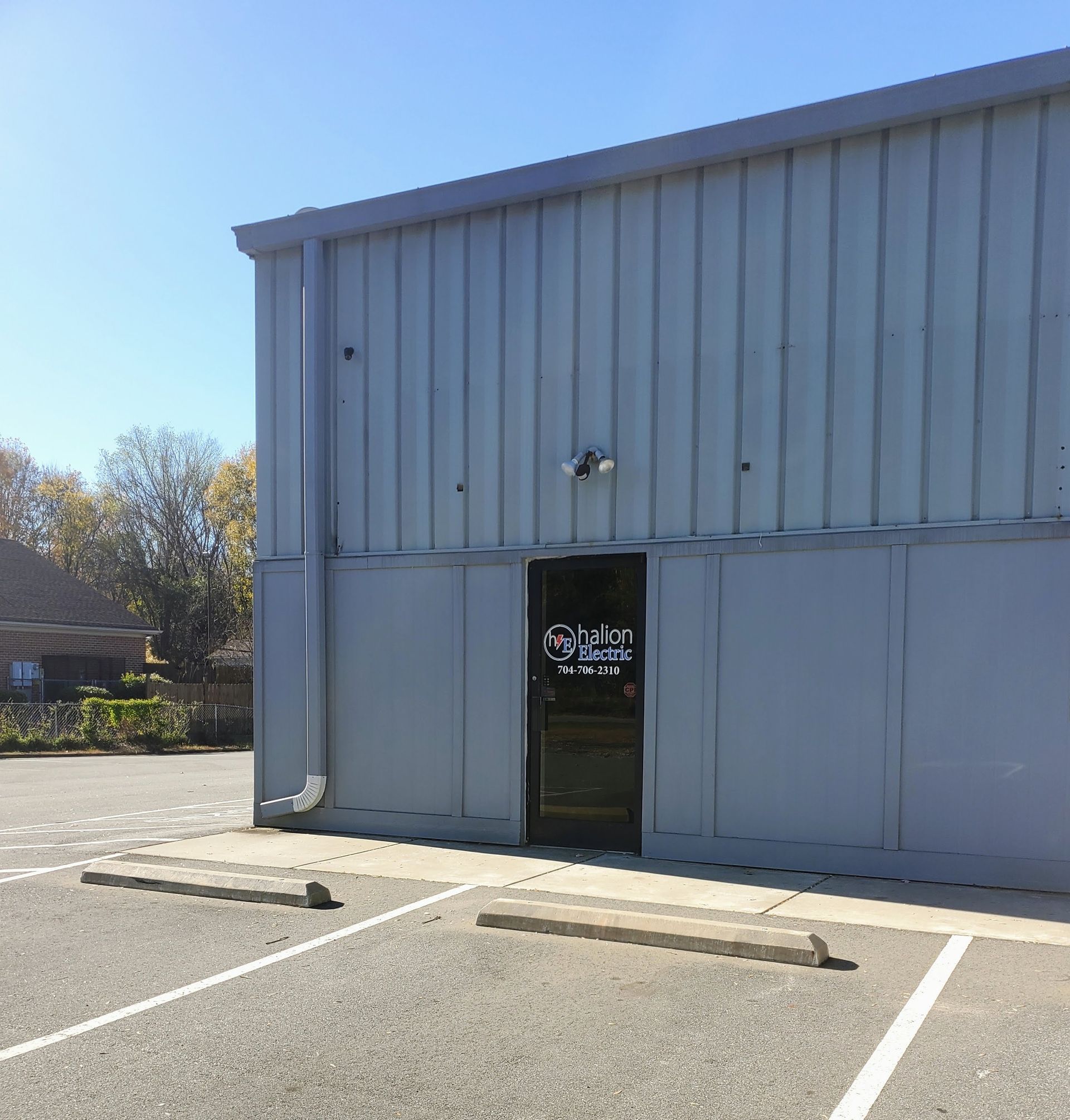 Gray metal building with a black glass entrance door and empty parking spaces in front