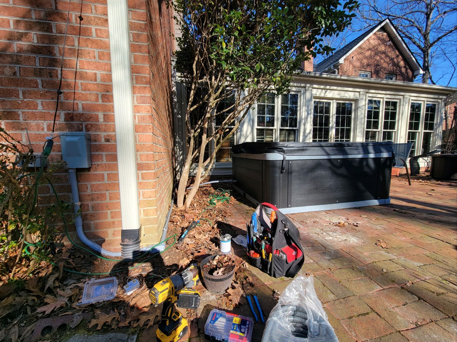 Backyard patio with a large black storage bin, potted bags, and brick house walls in sunlight