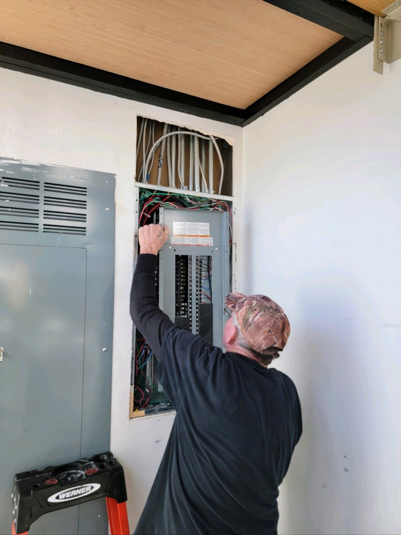 Technician working inside an open electrical panel in a utility room
