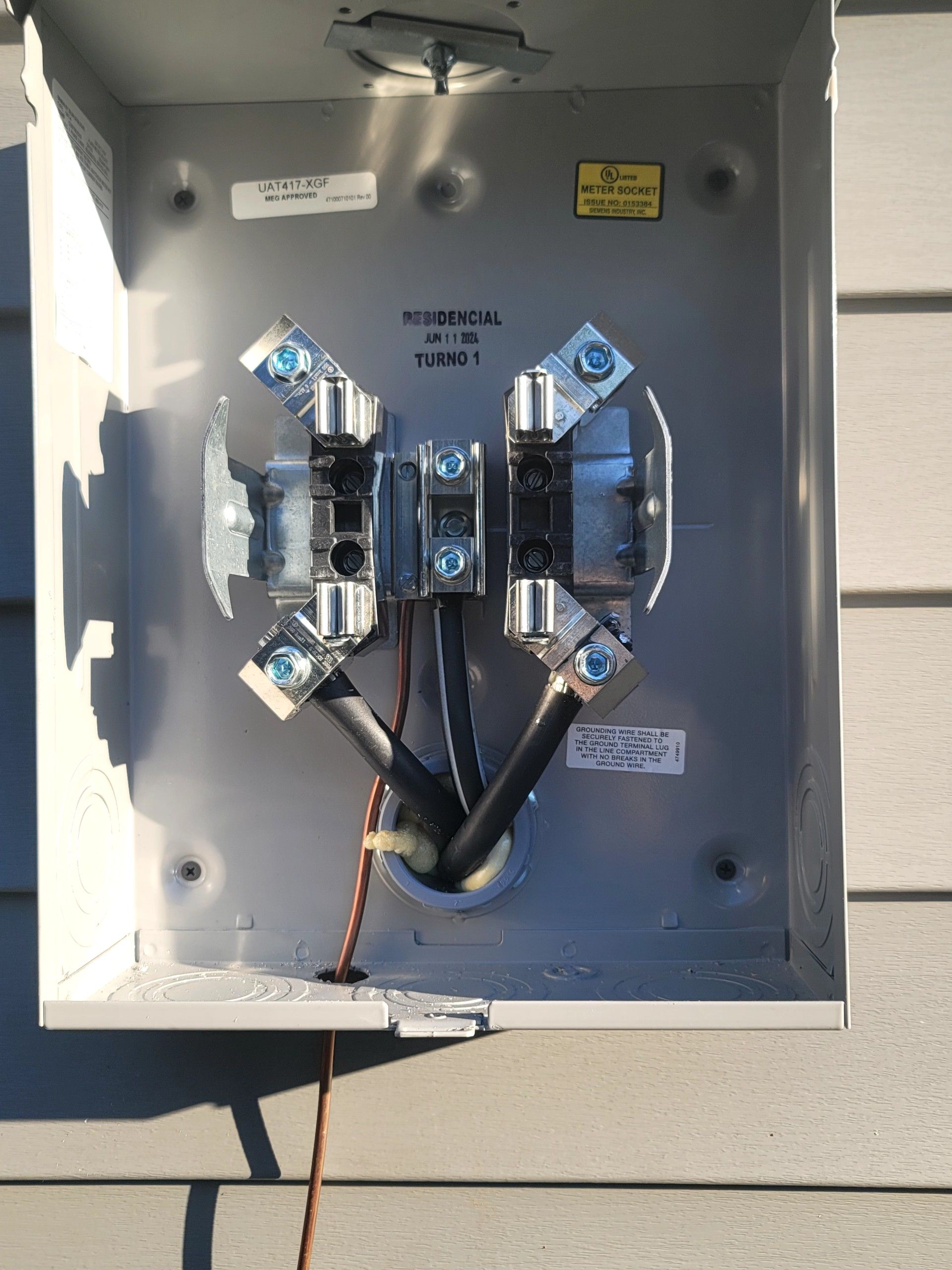 Open electrical meter panel with wires and two meter sockets on a gray wall