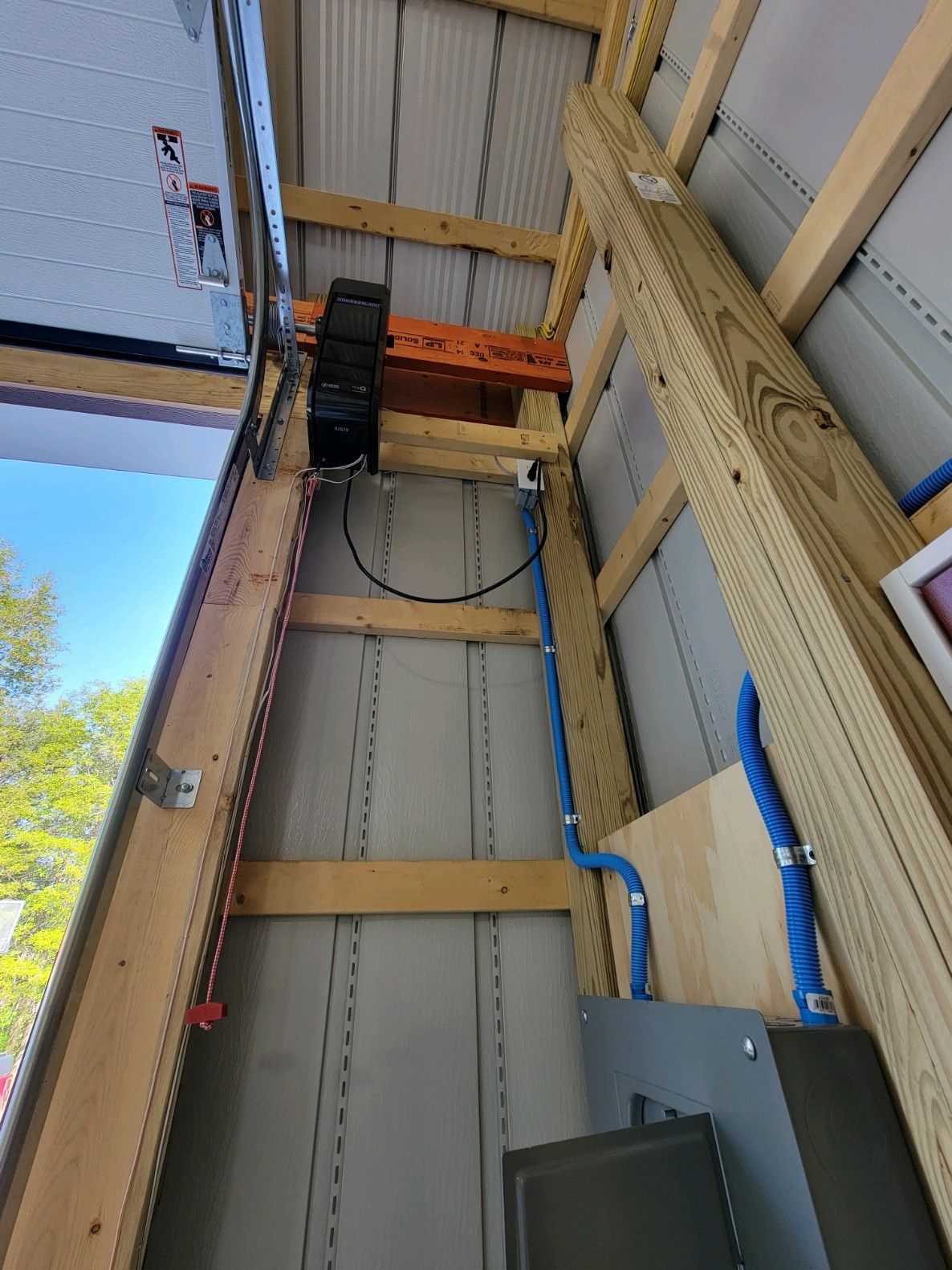 Indoor utility wall with exposed beams, wiring, and a mounted black electrical box near a metal ceiling.