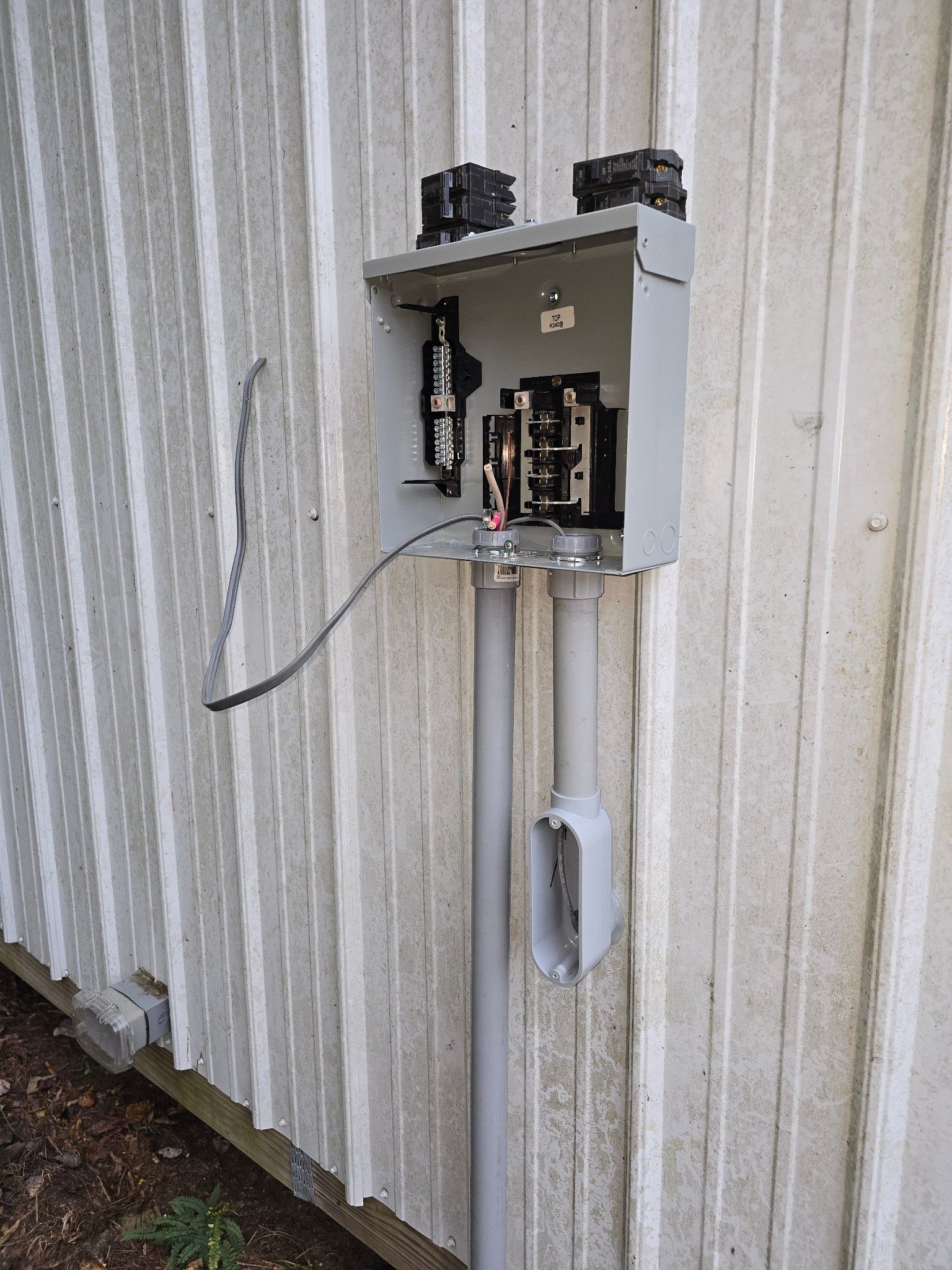 Open electrical control box mounted on a corrugated metal wall, with exposed wiring.