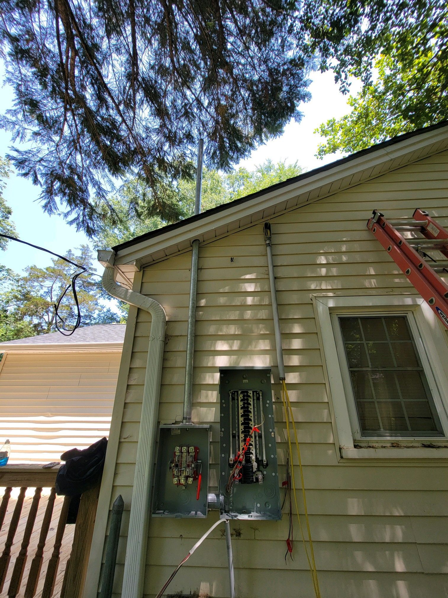 House exterior with an open window, ladder, and hanging tools under trees