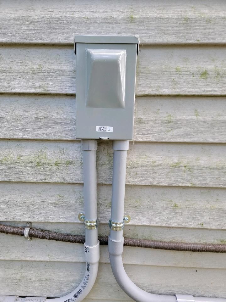 Gray electrical box with two conduit pipes on an exterior house wall