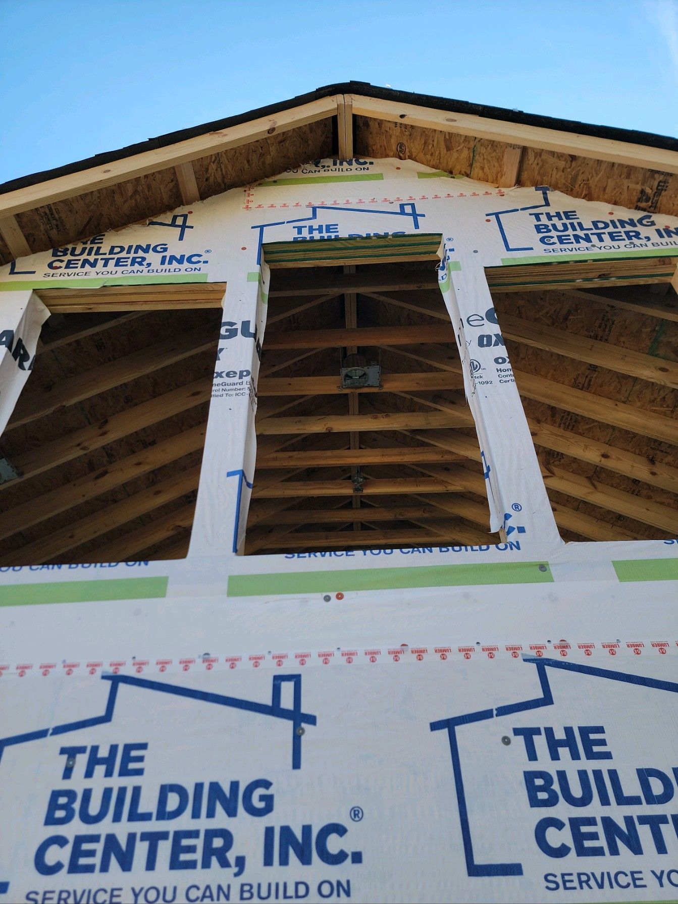 Partially built house exterior with exposed wooden framing and Building Center, Inc. house wrap under a blue sky