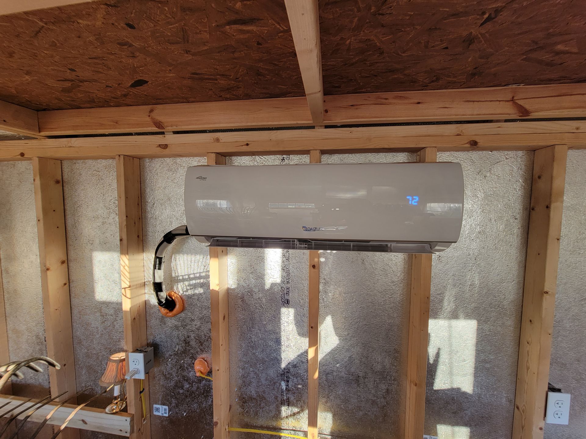 Wall-mounted mini-split air conditioner in an unfinished room with exposed wood framing and insulation.