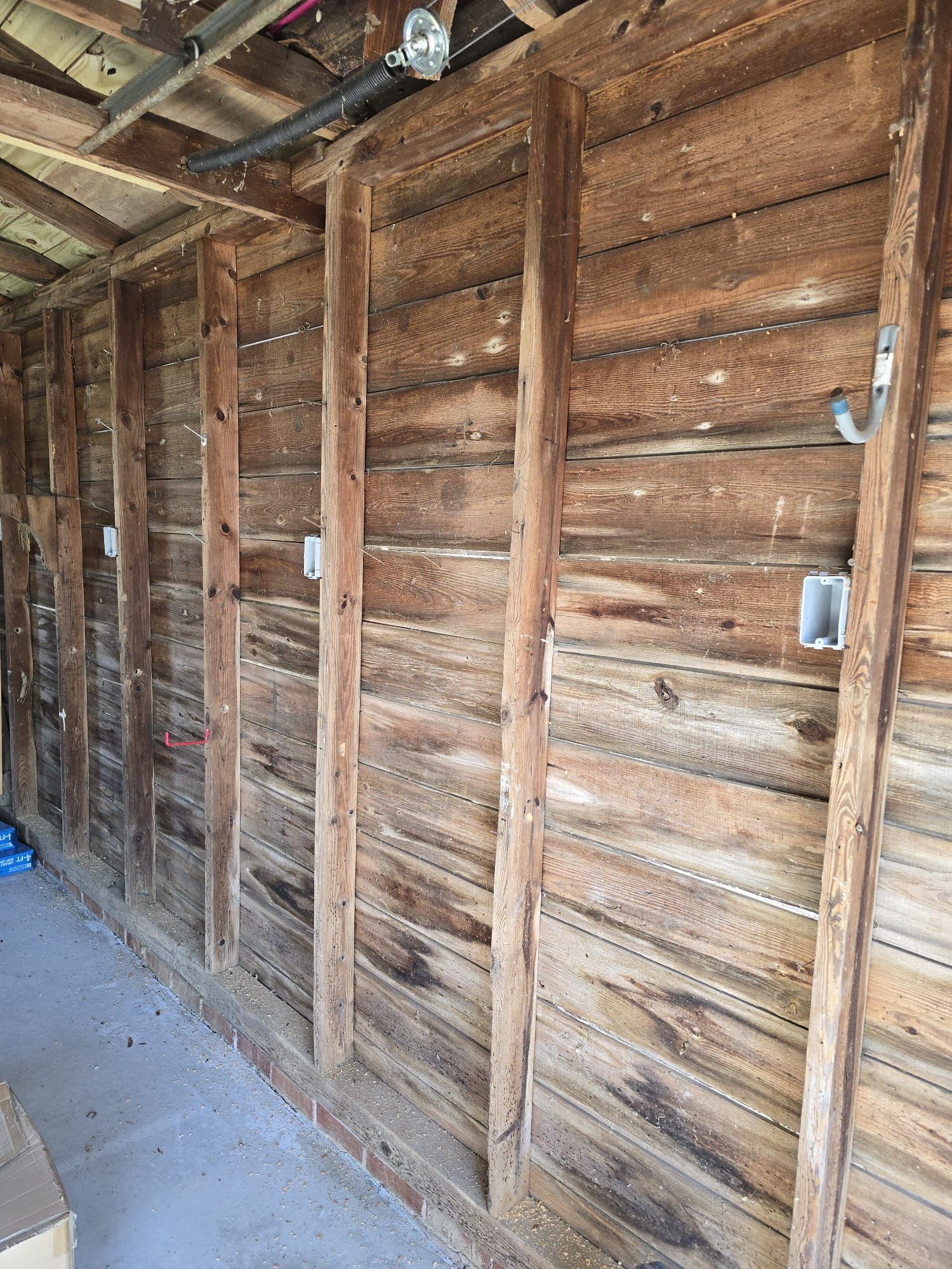 Interior of a rustic wooden shed wall with exposed studs and electrical outlets, lit by daylight.