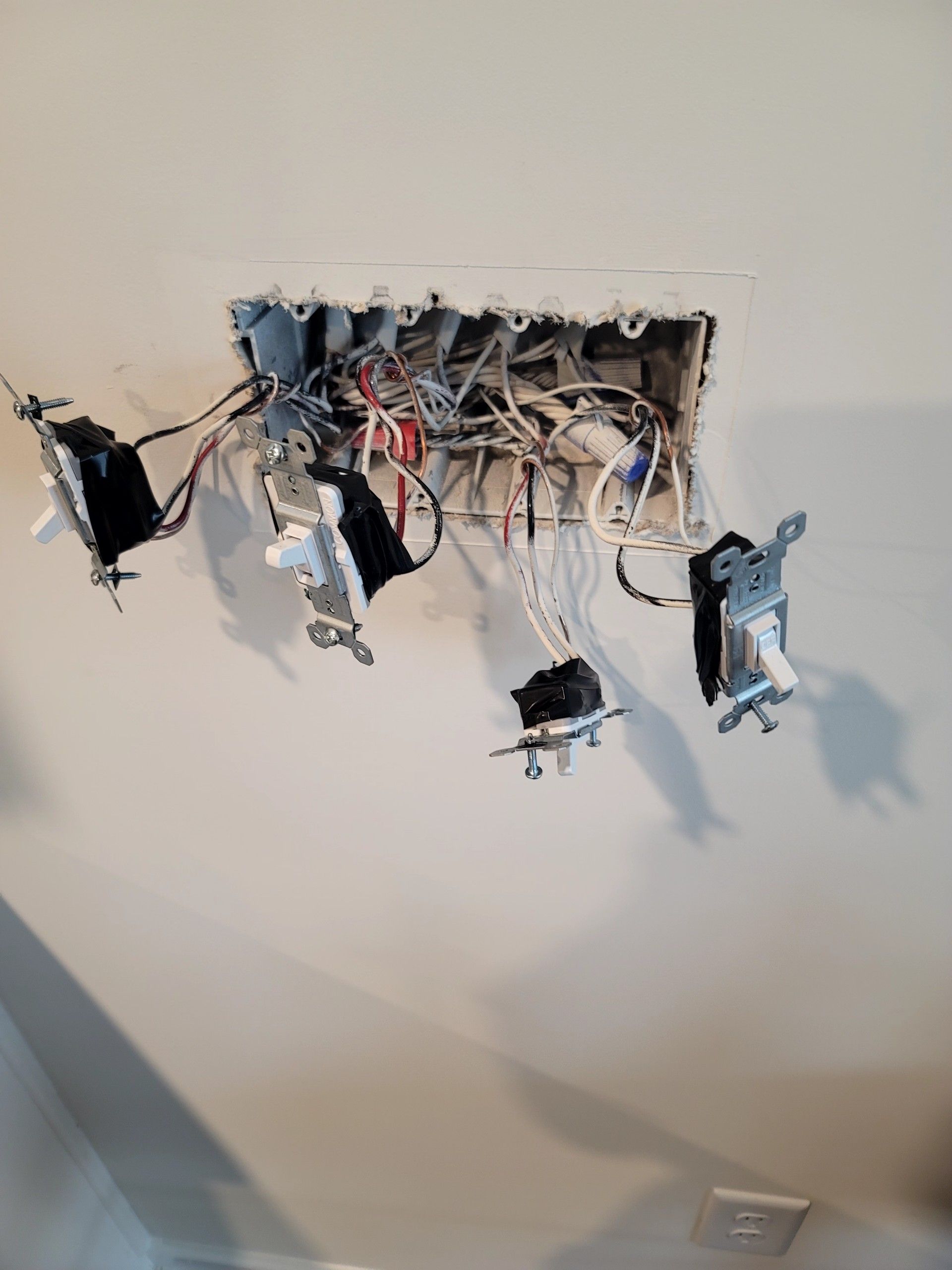 Exposed electrical wiring and open wall boxes in a damaged ceiling opening, with a loose light fixture hanging below.