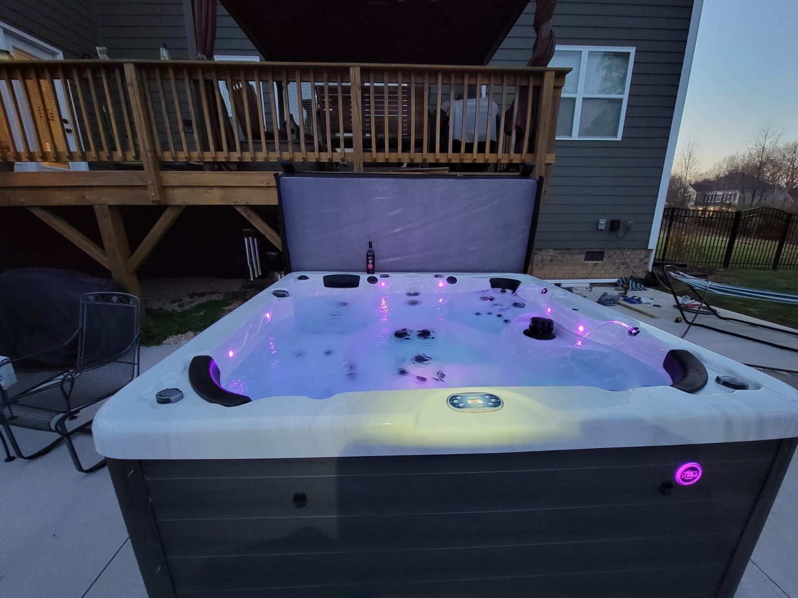 Lit hot tub glowing purple on a snowy deck beside a house at dusk