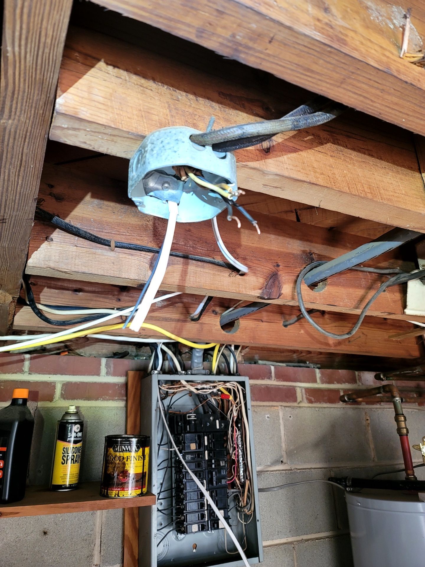 Attic ceiling with exposed wiring and a hanging electrical box above a brick wall.