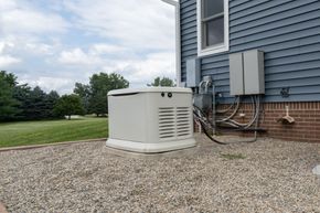 Outdoor home generator beside a blue house on a gravel yard