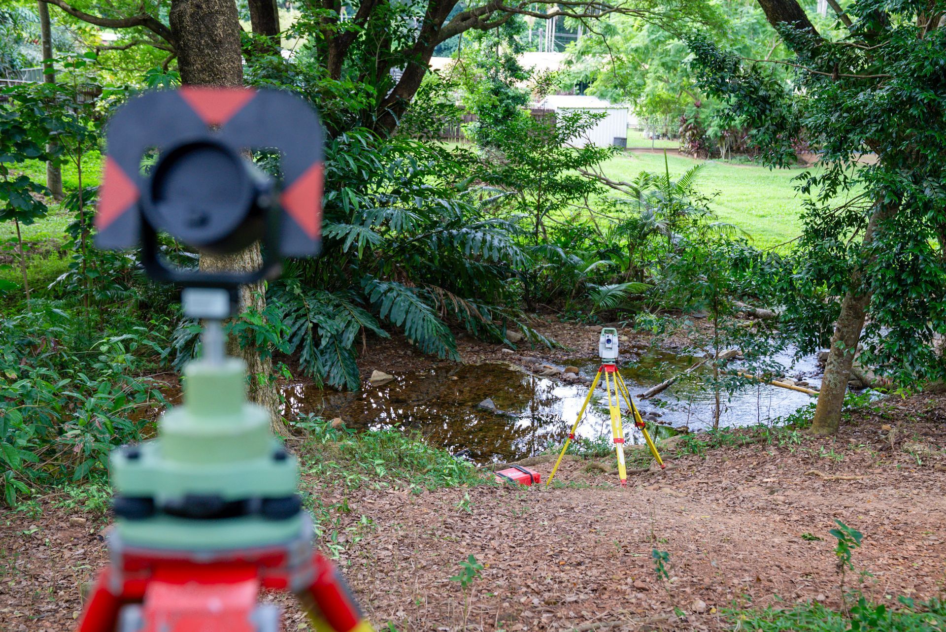 A Man Wearing A Hard Hat Is Looking Through A Theodolite While Holding A Laptop — TerraModus Surveying In Bayview Heights, QLD