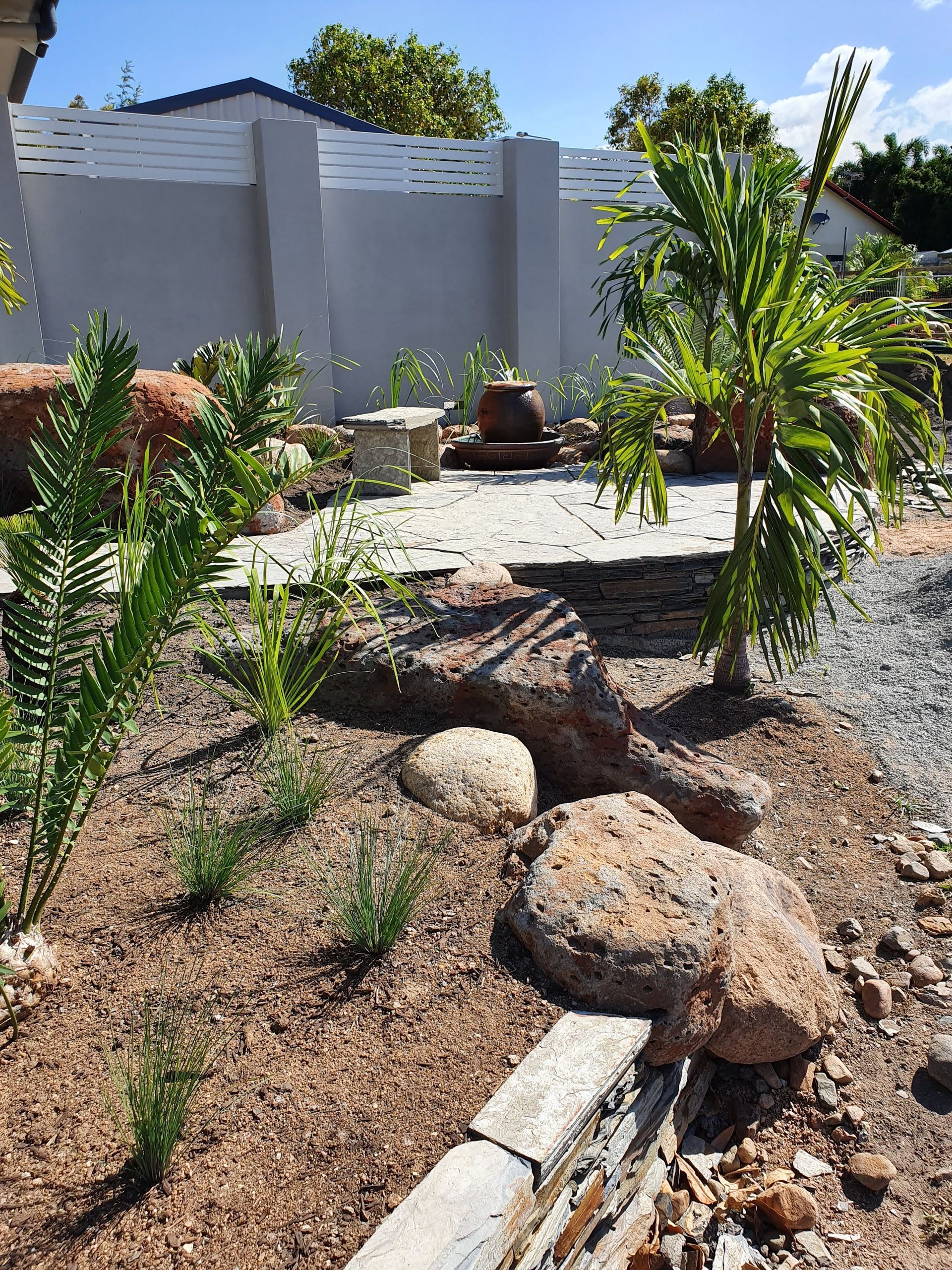 A Landscaped Garden Bed Featuring Mulch, Large Rocks, Ferns, and a Palm — High End Stone Masons in West End, QLD