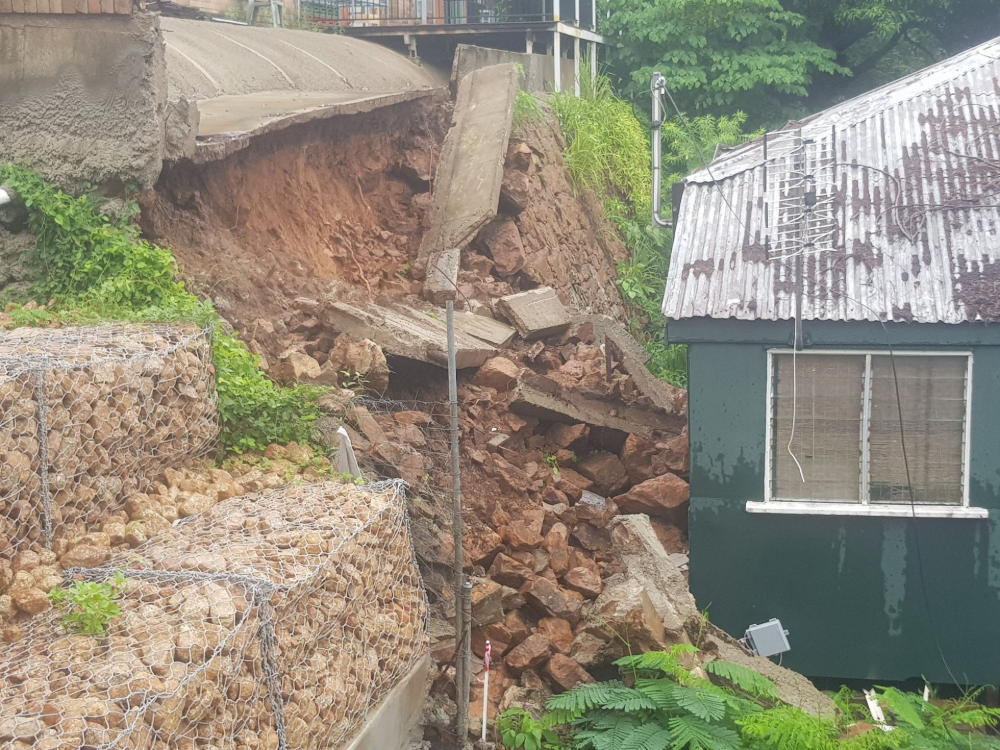 Collapsed hillside with debris beside a green building and gabion retaining wall— High End Stone Masons in West End, QLD