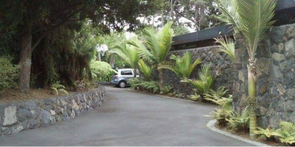 Curved driveway beside lush tropical plants and lava rock walls, leading to a white car in the distance — High End Stone Masons in West End, QLD