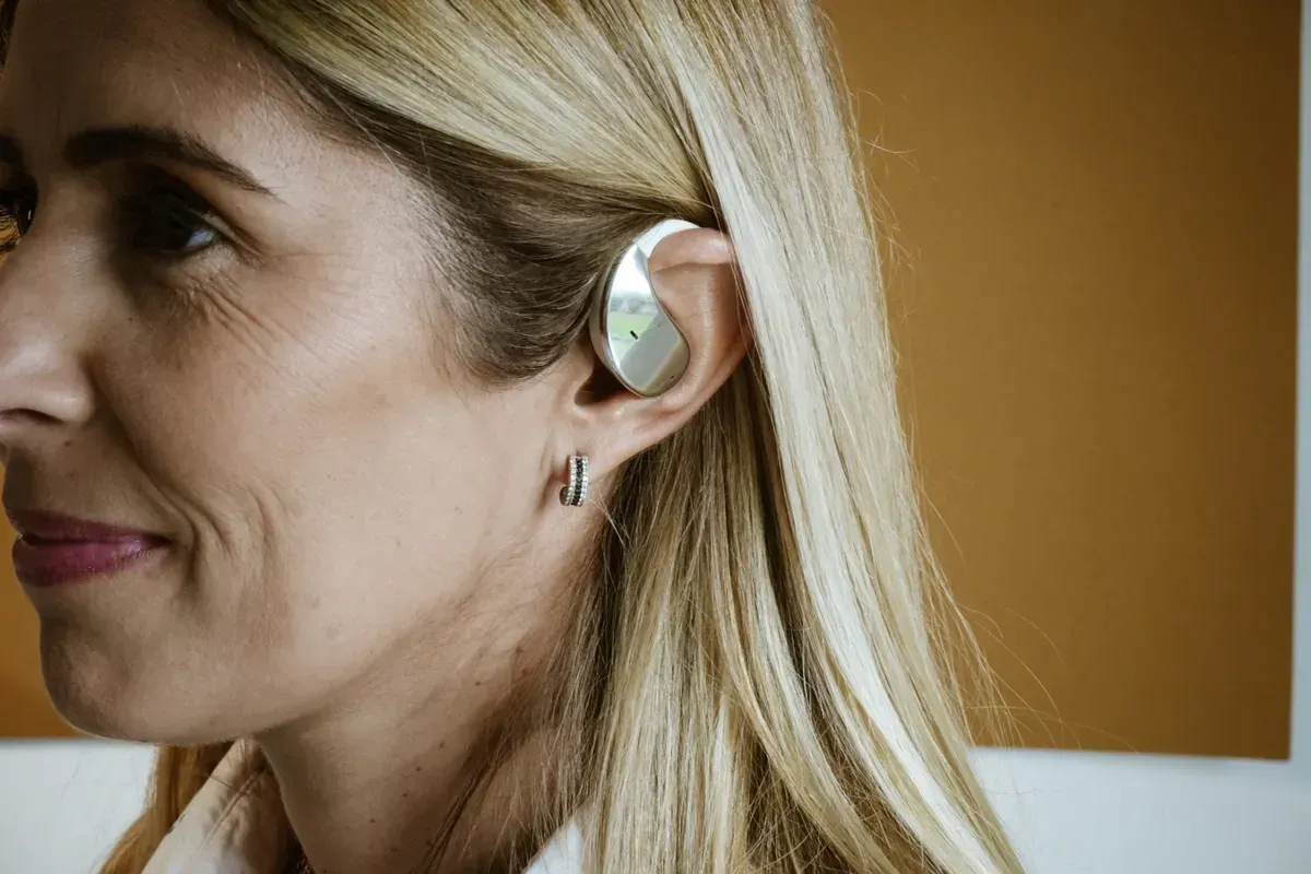 Auriculares inalámbricos blancos con estuche de carga; diseño de gancho para la oreja, detalles plateados.