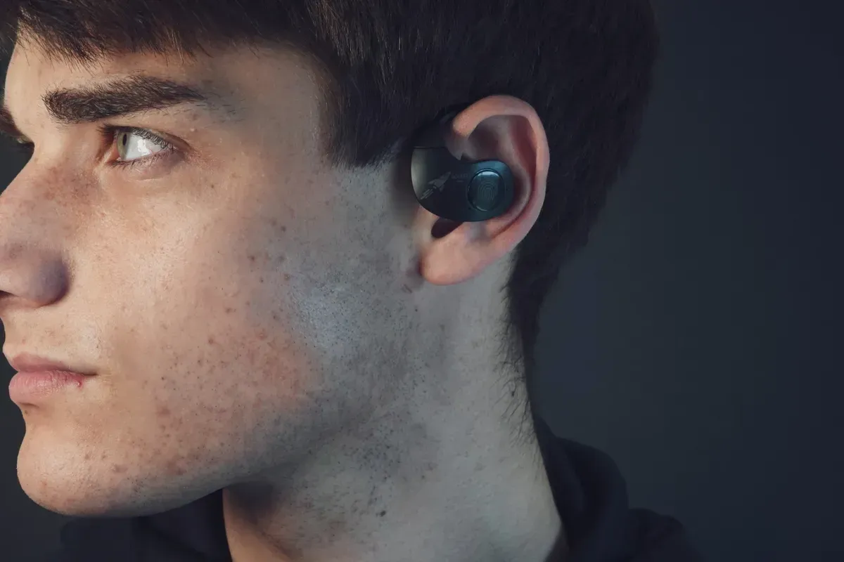 Auriculares y estuche de carga en color gris metalizado; los auriculares descansan sobre una superficie color bronce.