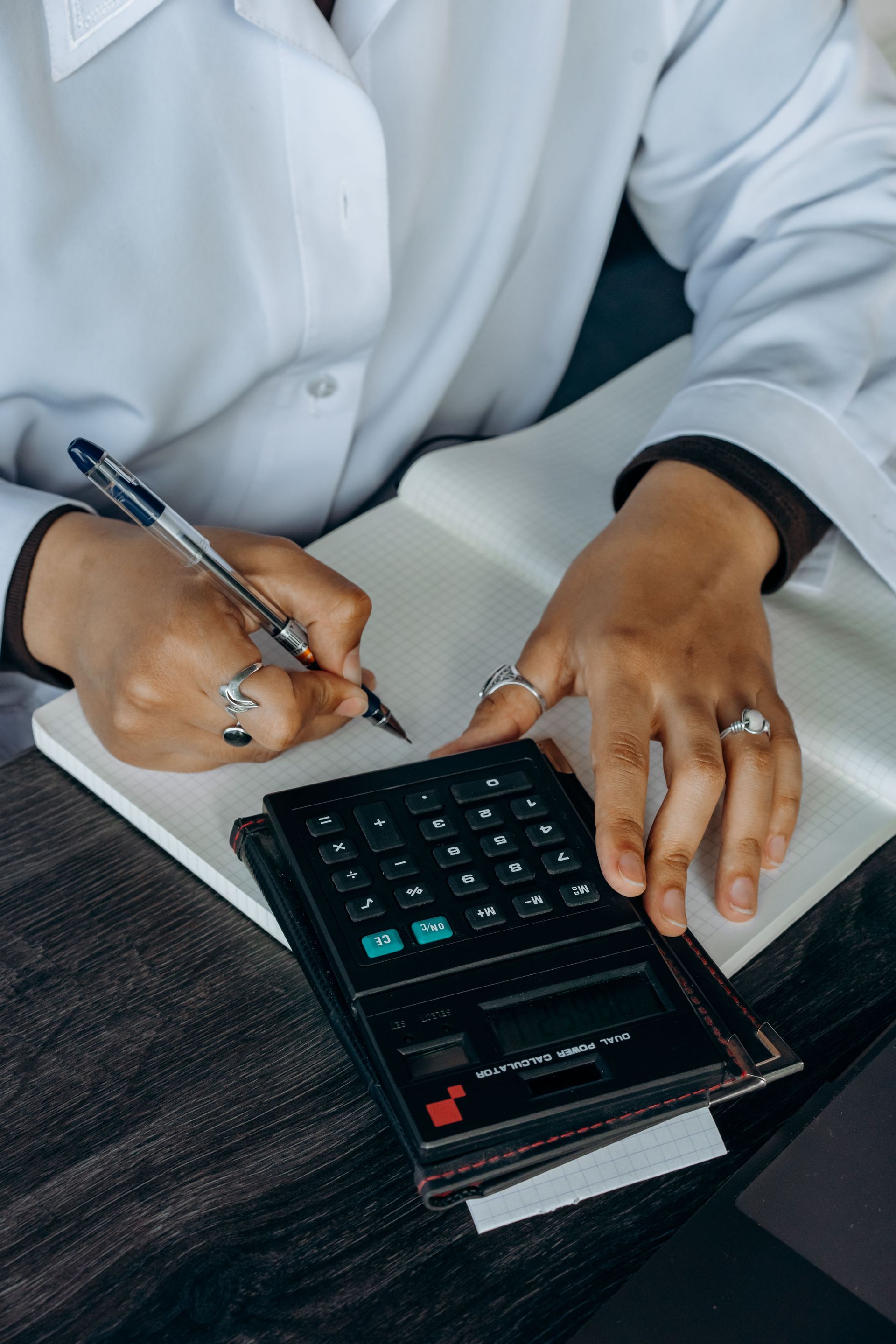 Hands writing in a notebook beside a calculator on a desk