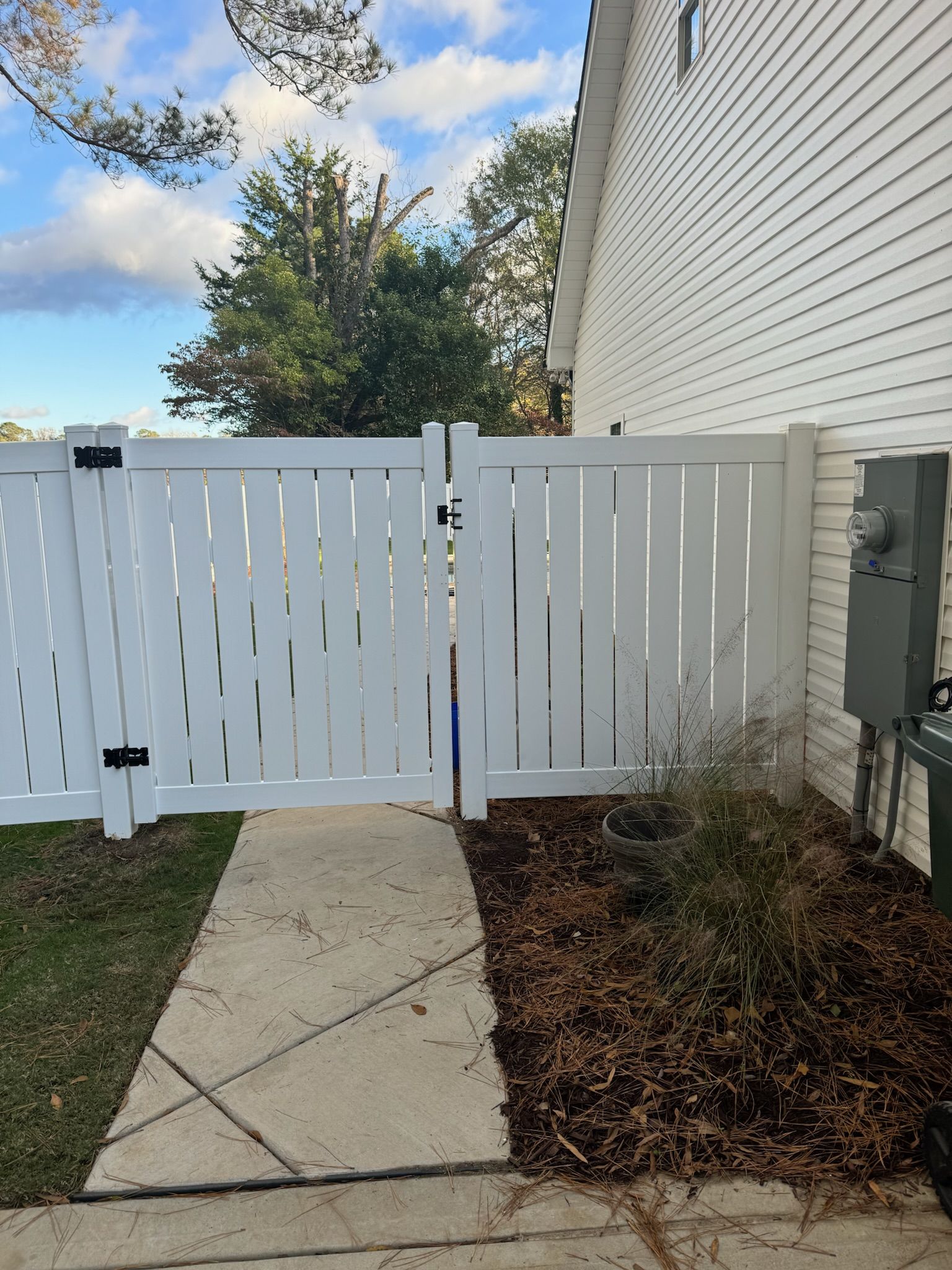 A white fence is sitting next to a sidewalk next to a house.