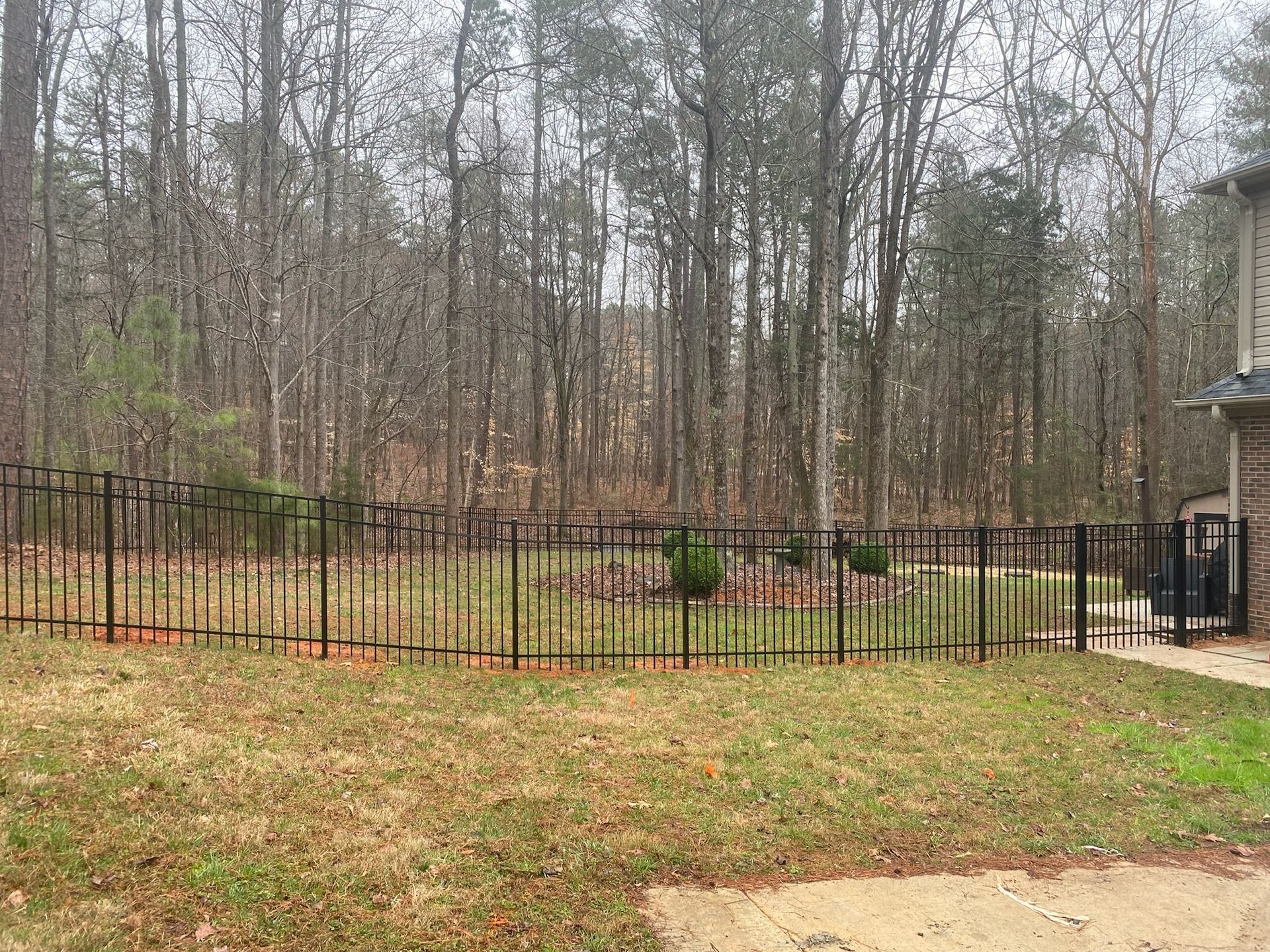 A black metal fence surrounds a grassy yard in front of a house.