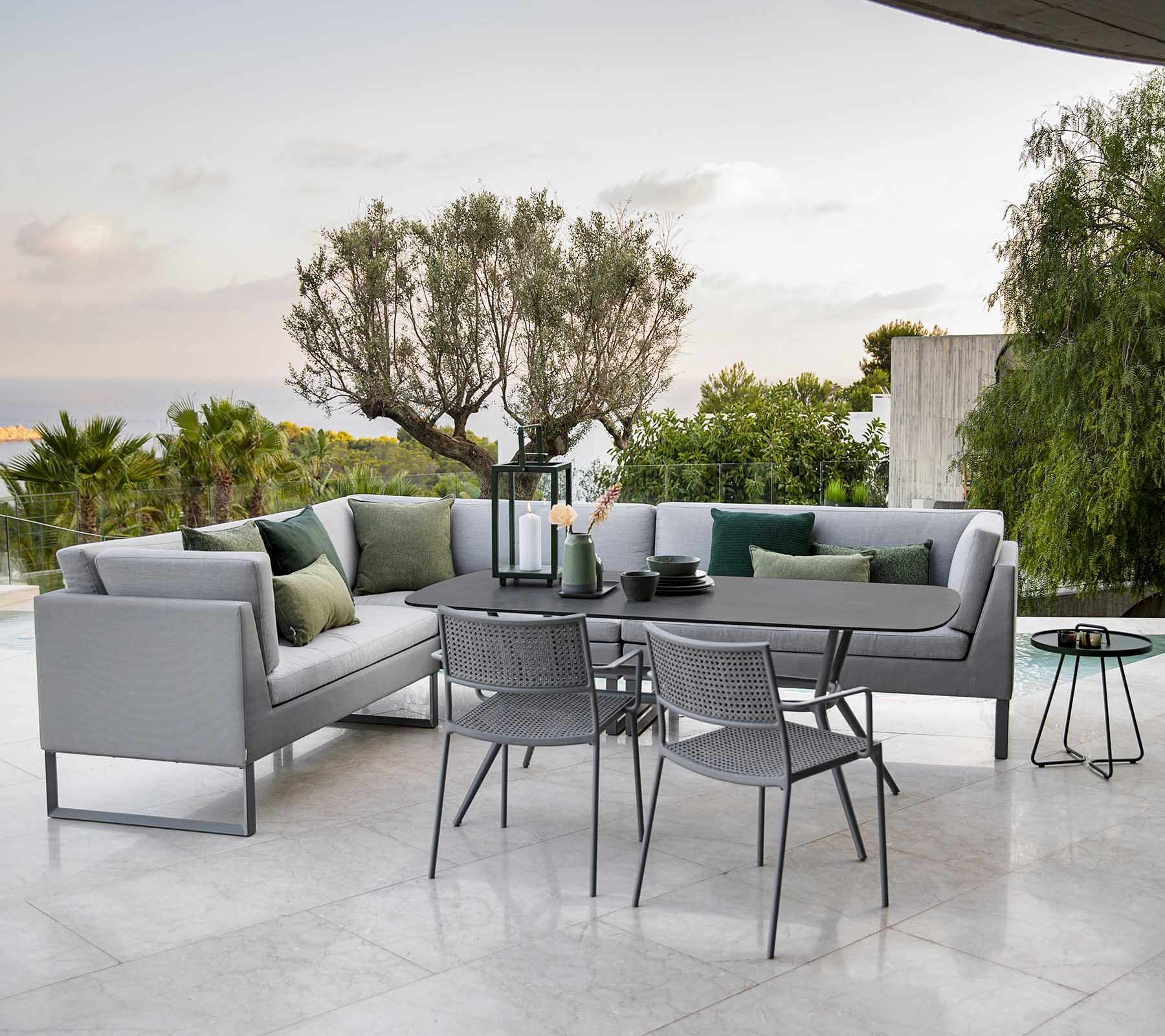 Moderne Außenterrasse mit grauer Ecksitzgruppe, schwarzen Stühlen und einem runden Tisch auf einer gefliesten Terrasse