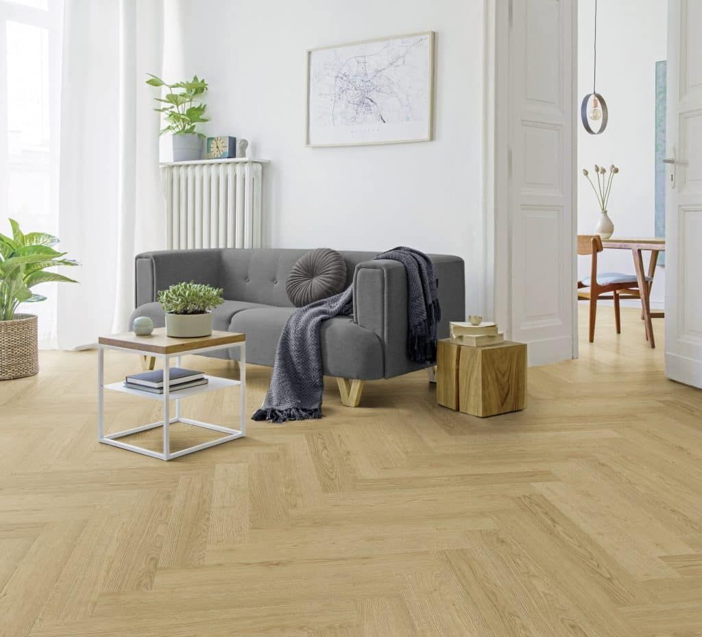 Helles Wohnzimmer mit grauem Sofa, hellem Holzboden, Couchtisch, Pflanzen und einer offenen Tür zum Essbereich