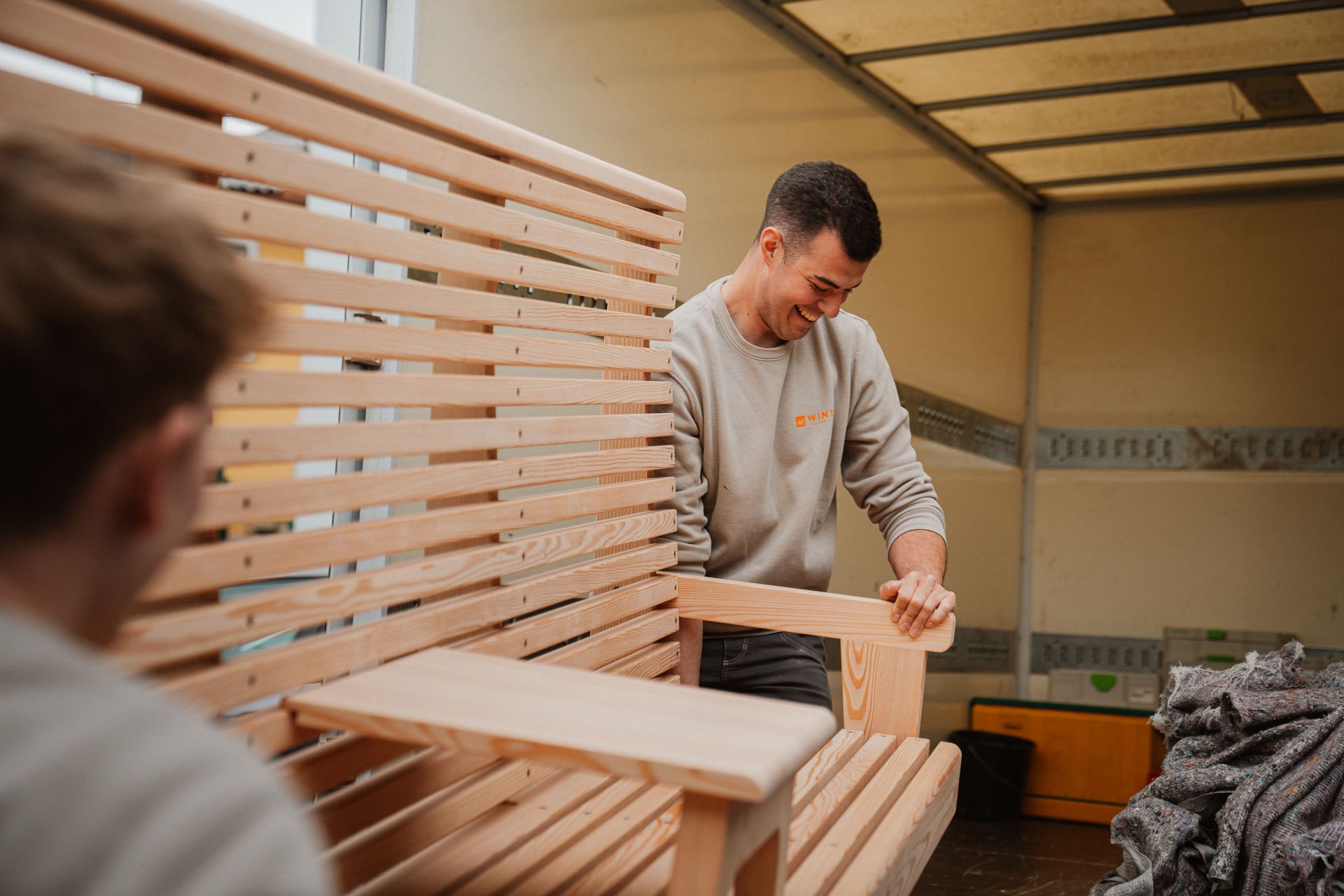 Ein Mann ordnet in einer Werkstatt neben einer halbfertigen Bank Holzlatten an.