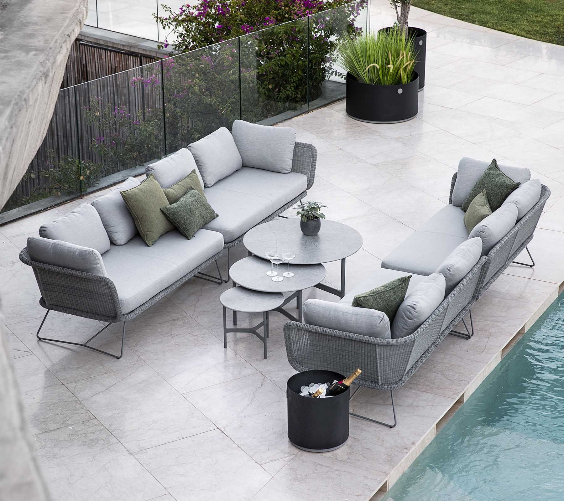 Graue Terrassensofa-Garnitur mit runden Tischen auf einer hellen Steinterrasse neben einem Pool