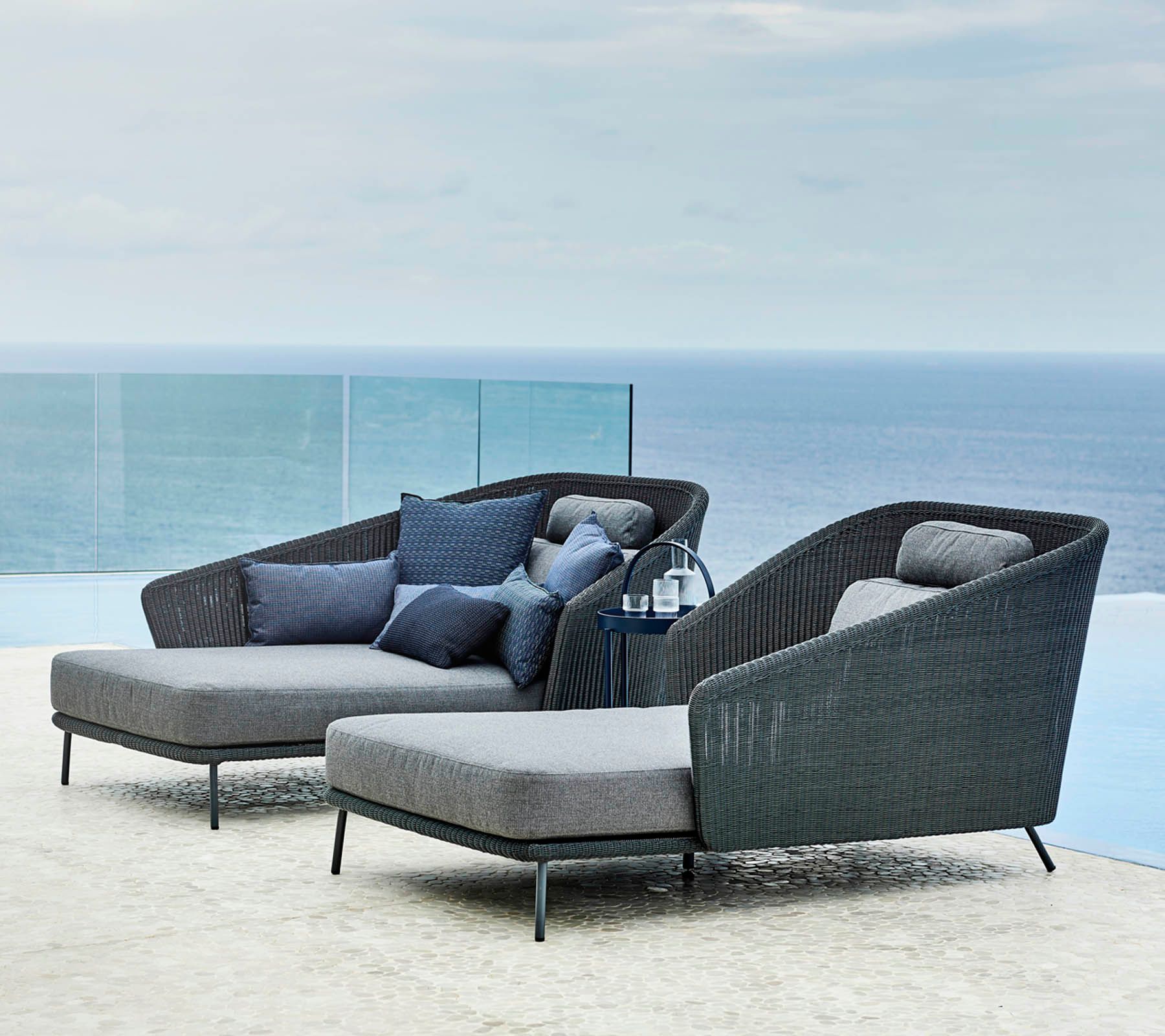 Moderne graue Outdoor-Loungesessel und ein passender Hocker auf einer Terrasse mit Blick auf das Meer