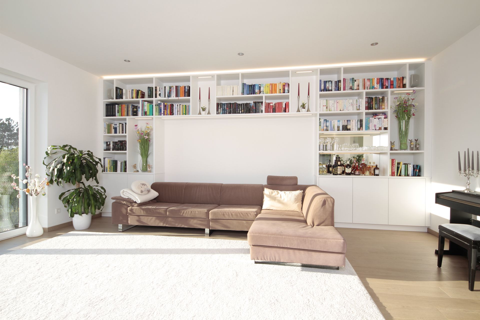 Helles Wohnzimmer mit eingebauten Bücherregalen, braunem Sofa, beiger Chaiselongue und großen Fenstern