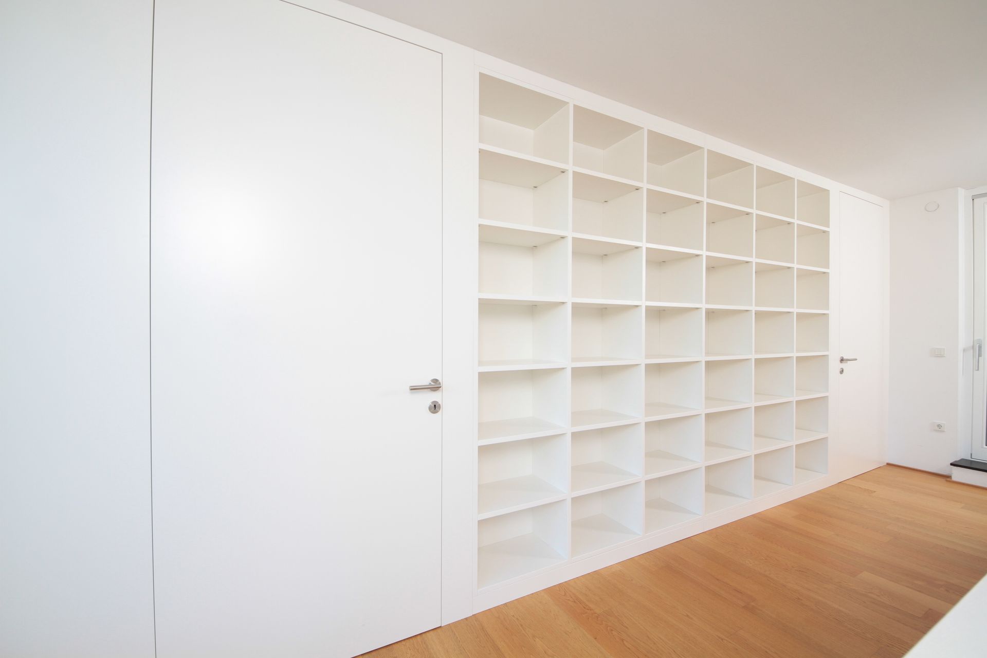 Ein helles, weißes Zimmer mit eingebauten weißen Regalen und Holzboden, gesehen aus einer Ecke.